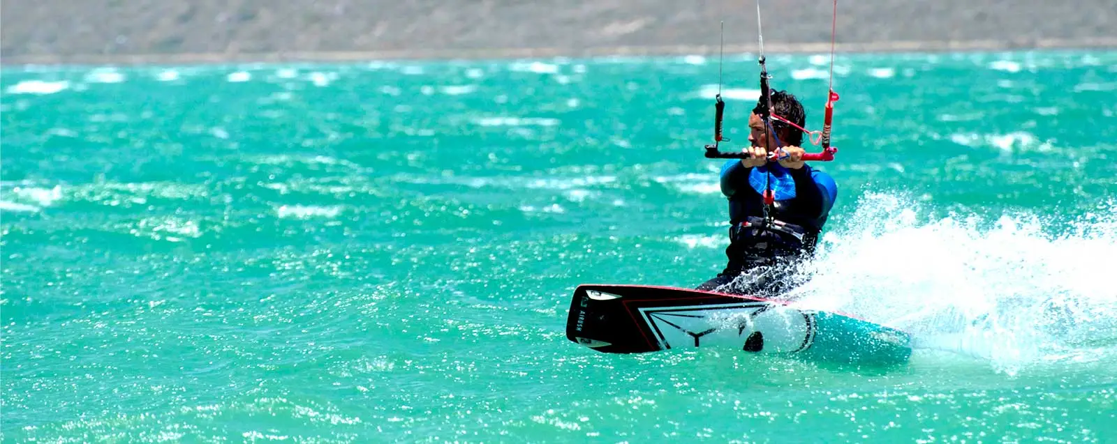 Kitesurfer gleitet mit Board durch türkisfarbenes Wasser, Gischt spritzt auf