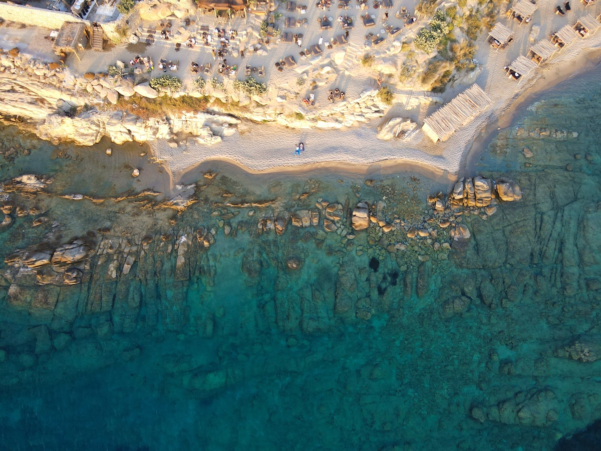 Aerial view of sunbathers, umbrellas, and turquoise water along a Mykonos beach