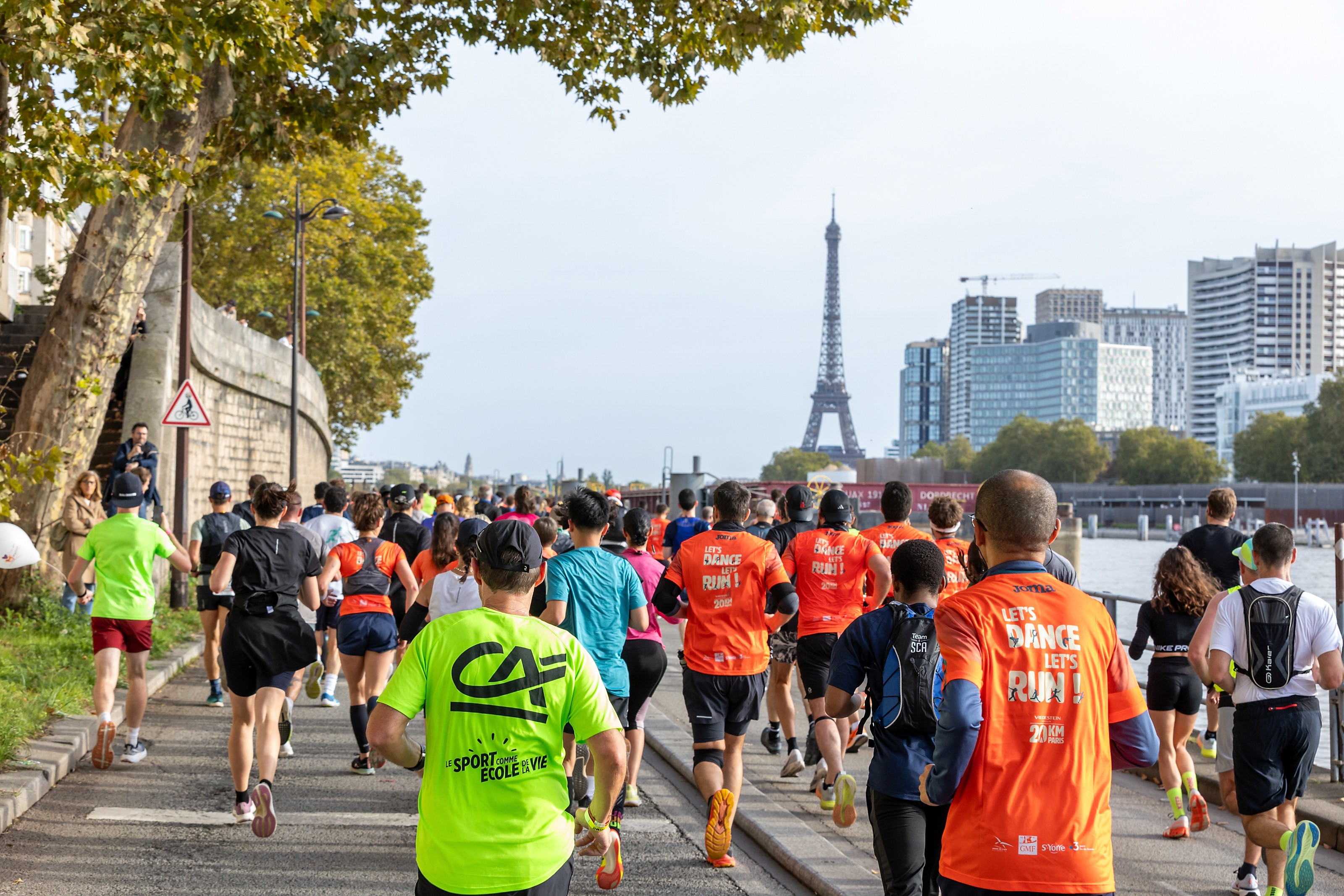 Groupe de coureurs participant à une course, avec la Tour Eiffel en arrière-plan et des arbres sur le côté de la route.