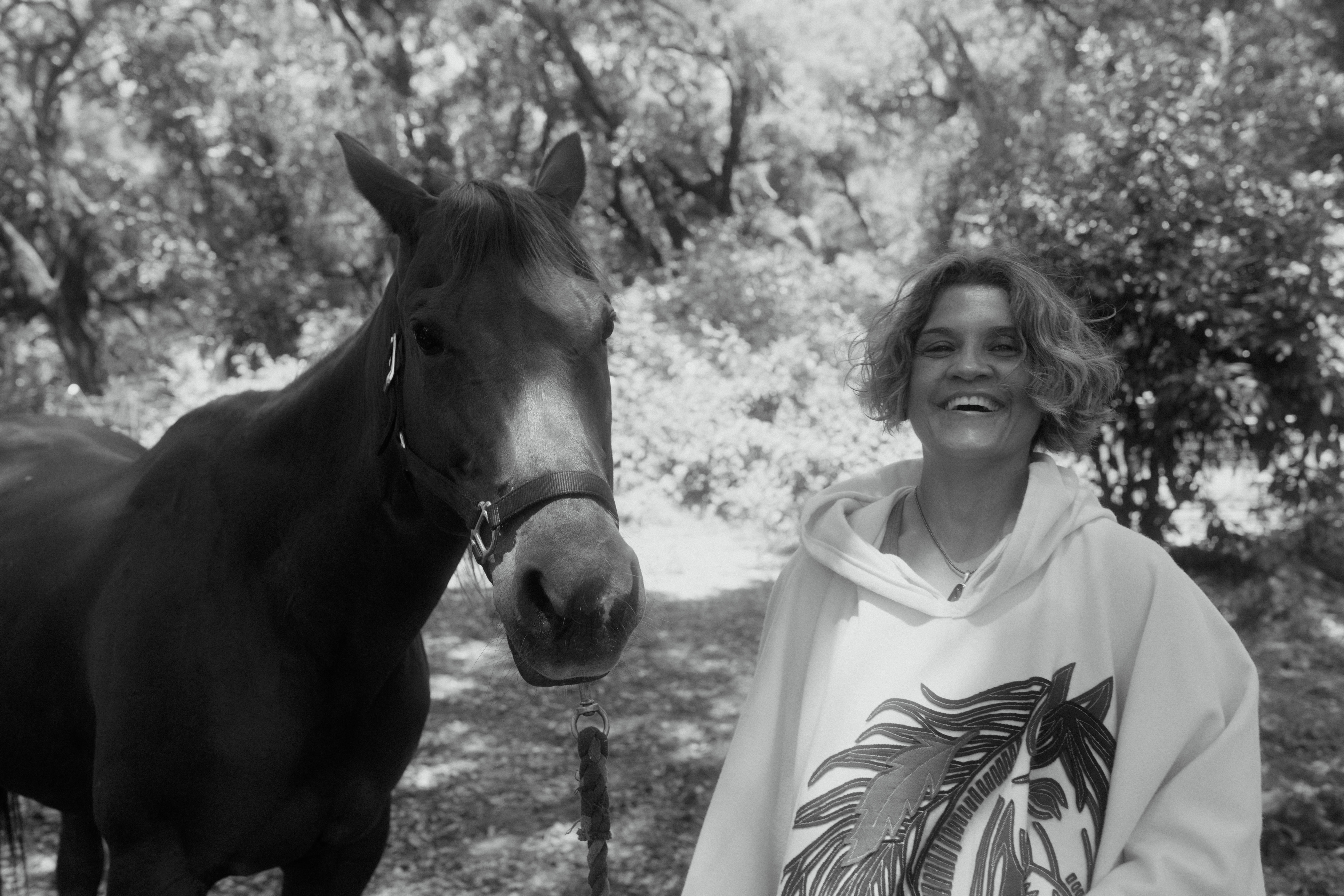 Sonia smiling beside her horse Corona in black and white, representing their sacred partnership