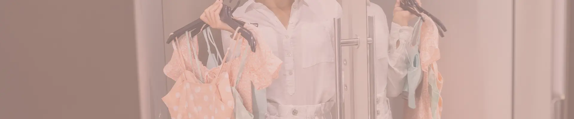 Woman holding up dresses on hangers while comparing options in a fitting room—illustrating product research and evaluating choices before making an online purchase.