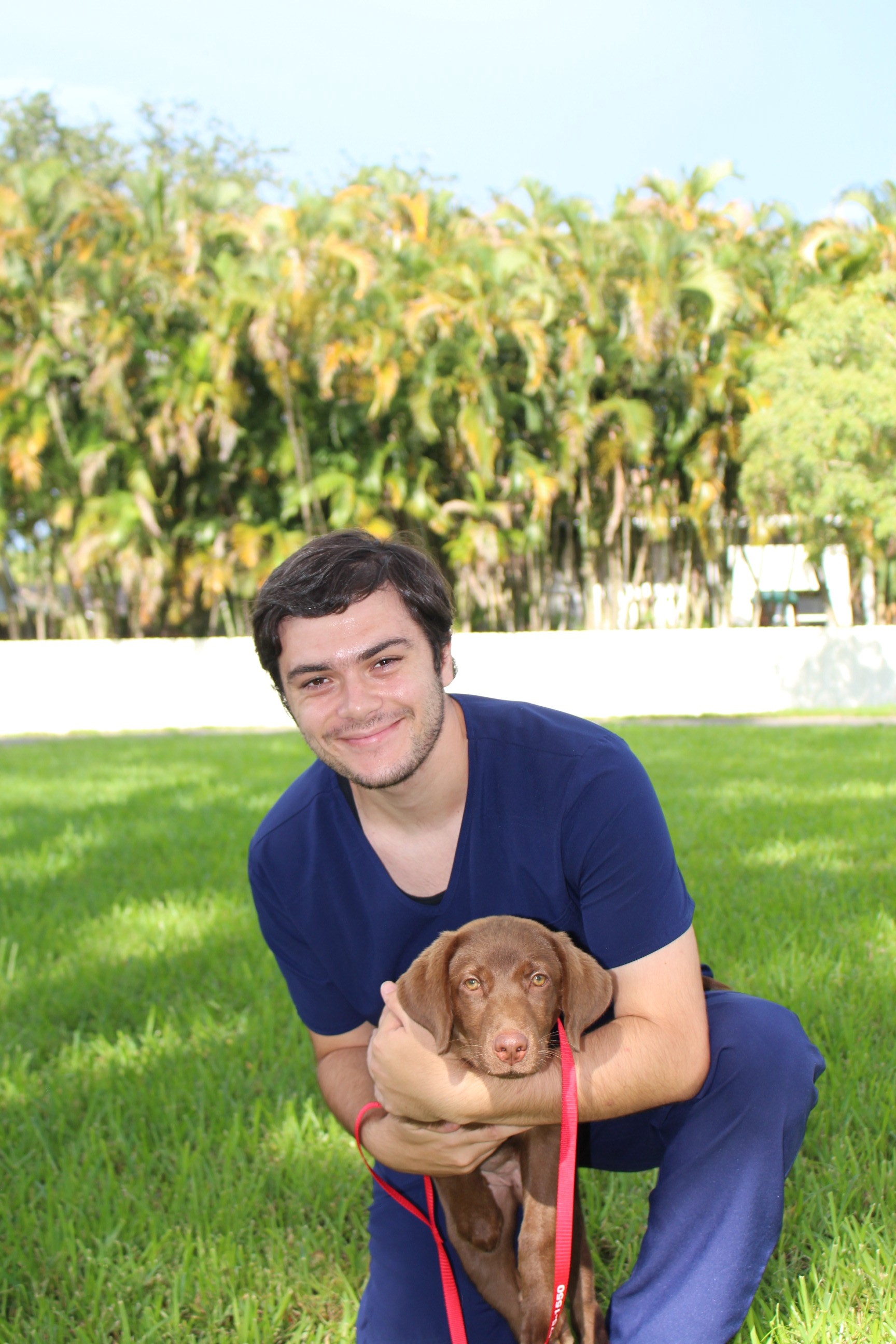 zack kneeling on the grass with a vizsla puppy