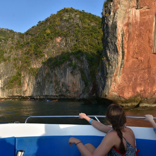 在晴朗的天空下，一个人在船上凝望着岩石陡壁和绿色植物。