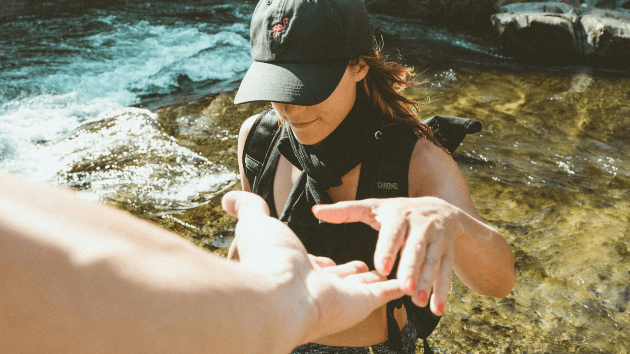 A woman reaching out her hand for help while crossing a river, symbolizing the importance of support and flexibility in overcoming challenges, much like real-time wage solutions.