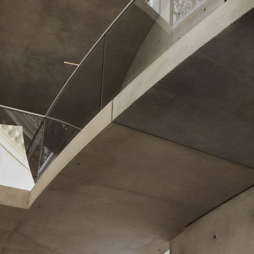 Modern interior with concrete walls and ceiling, glass railing, and metal supports viewed from below.