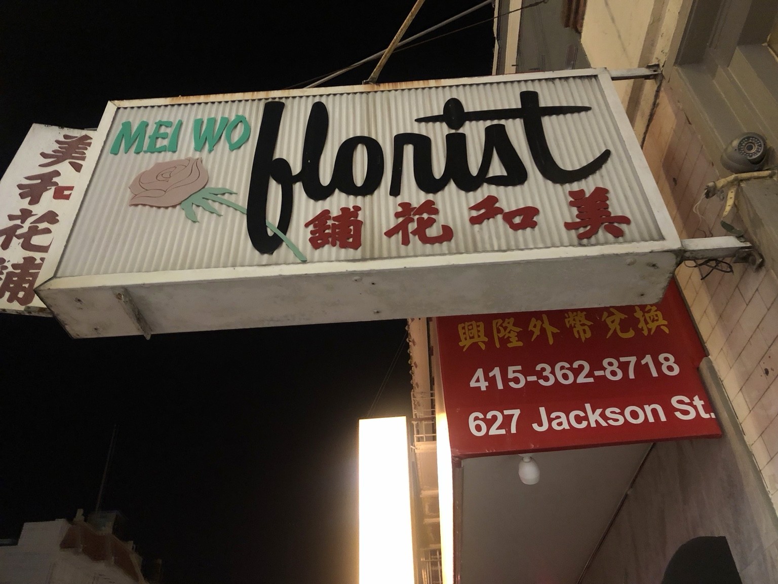 Mei Wo florist sign with script lettering and a pink rose, photographed at night