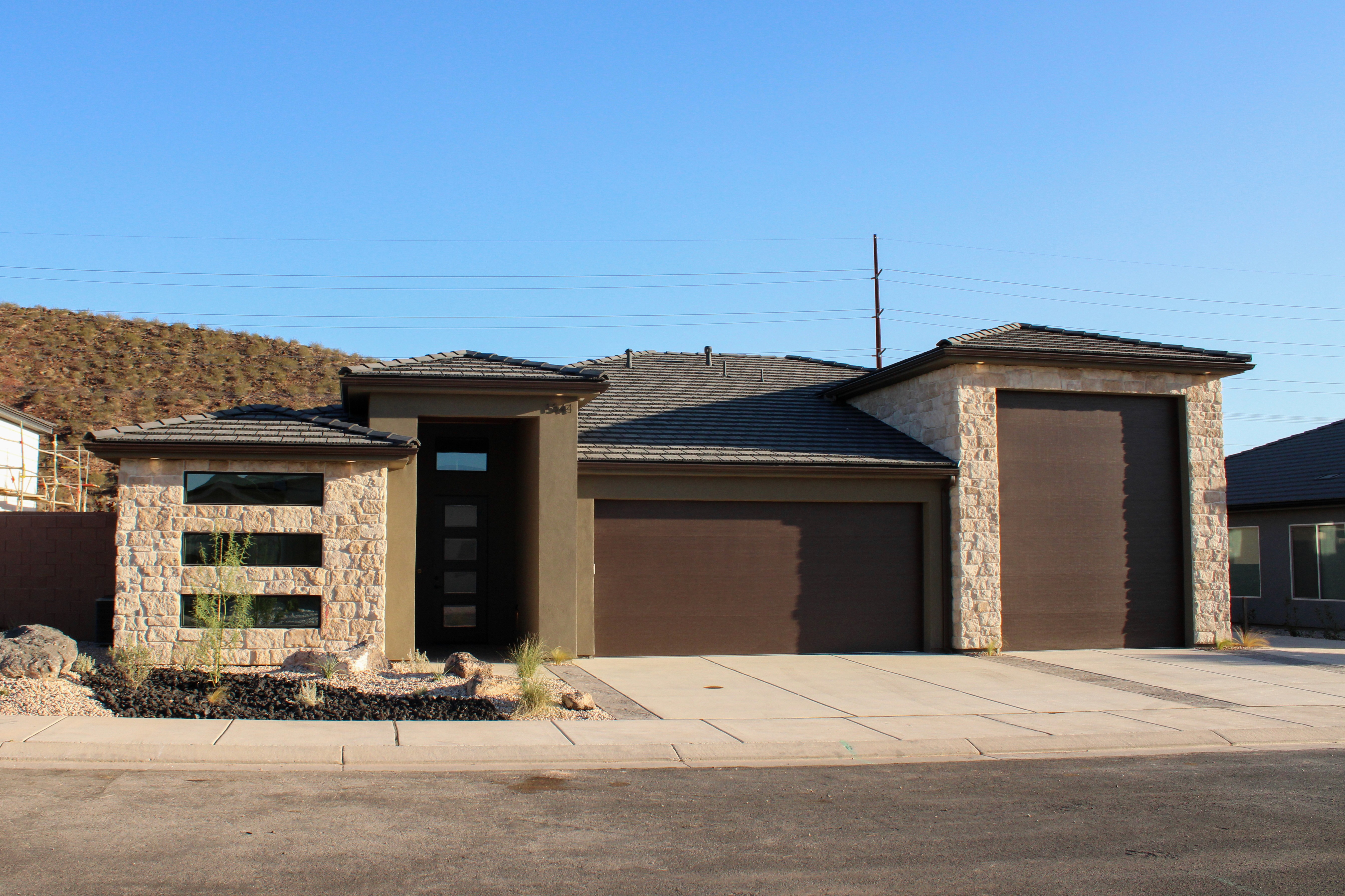 Southern Utah home exterior featuring green-toned stucco, natural stone, and brown garage doors designed to complement the desert surroundings.