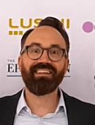 Editorial portrait of a young man with wavy hair in a knit sweater, looking over his shoulder in soft light.