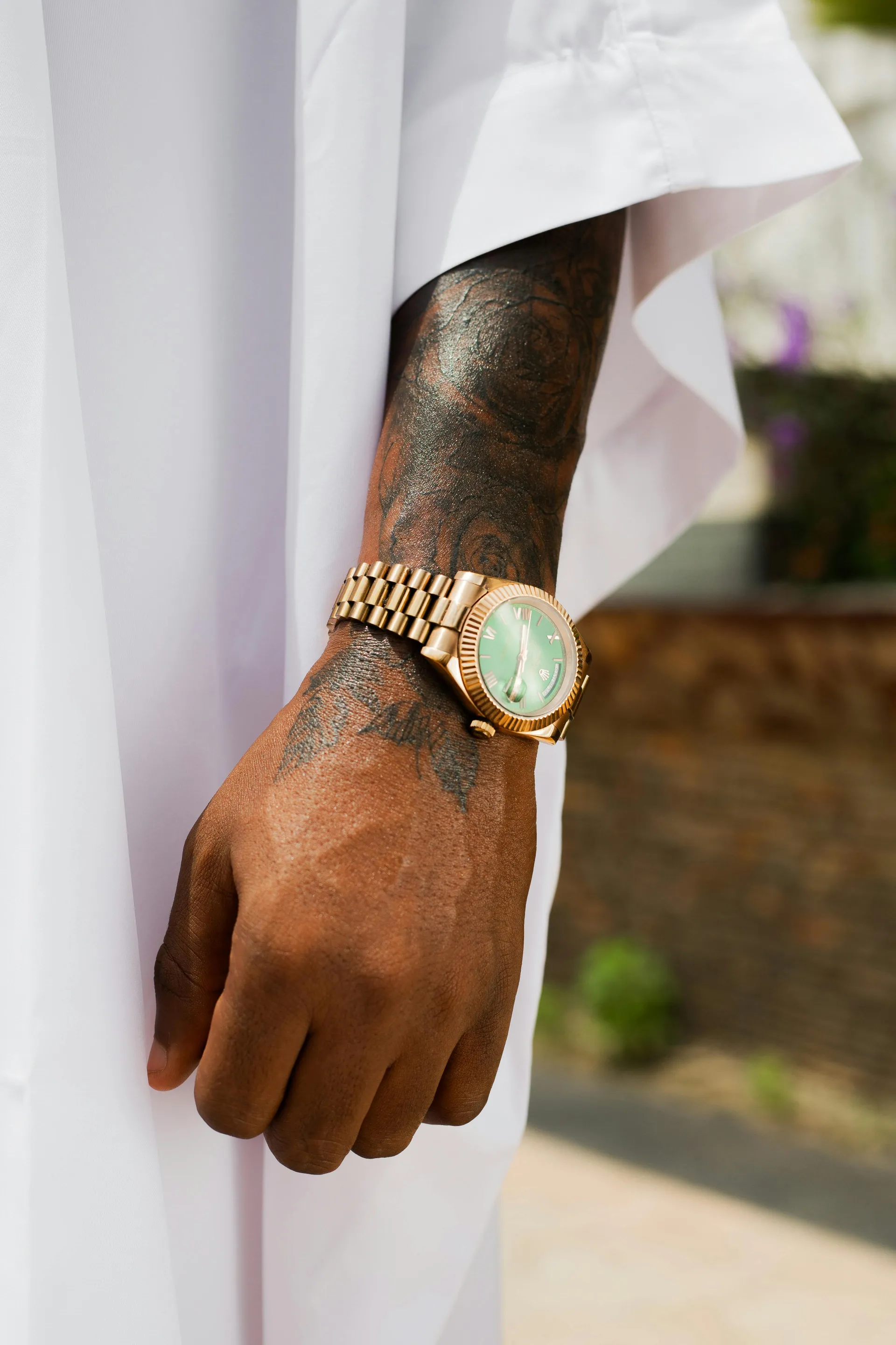 Gold watch with diamond bezel and Roman numeral dial on a brown leather strap on a wrist.