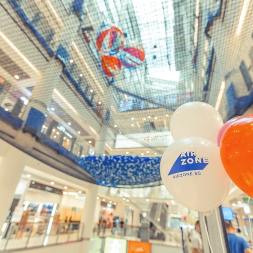 View of an indoor shopping mall with netting overhead, colorful balls suspended, and balloons labeled "AIRZONE".