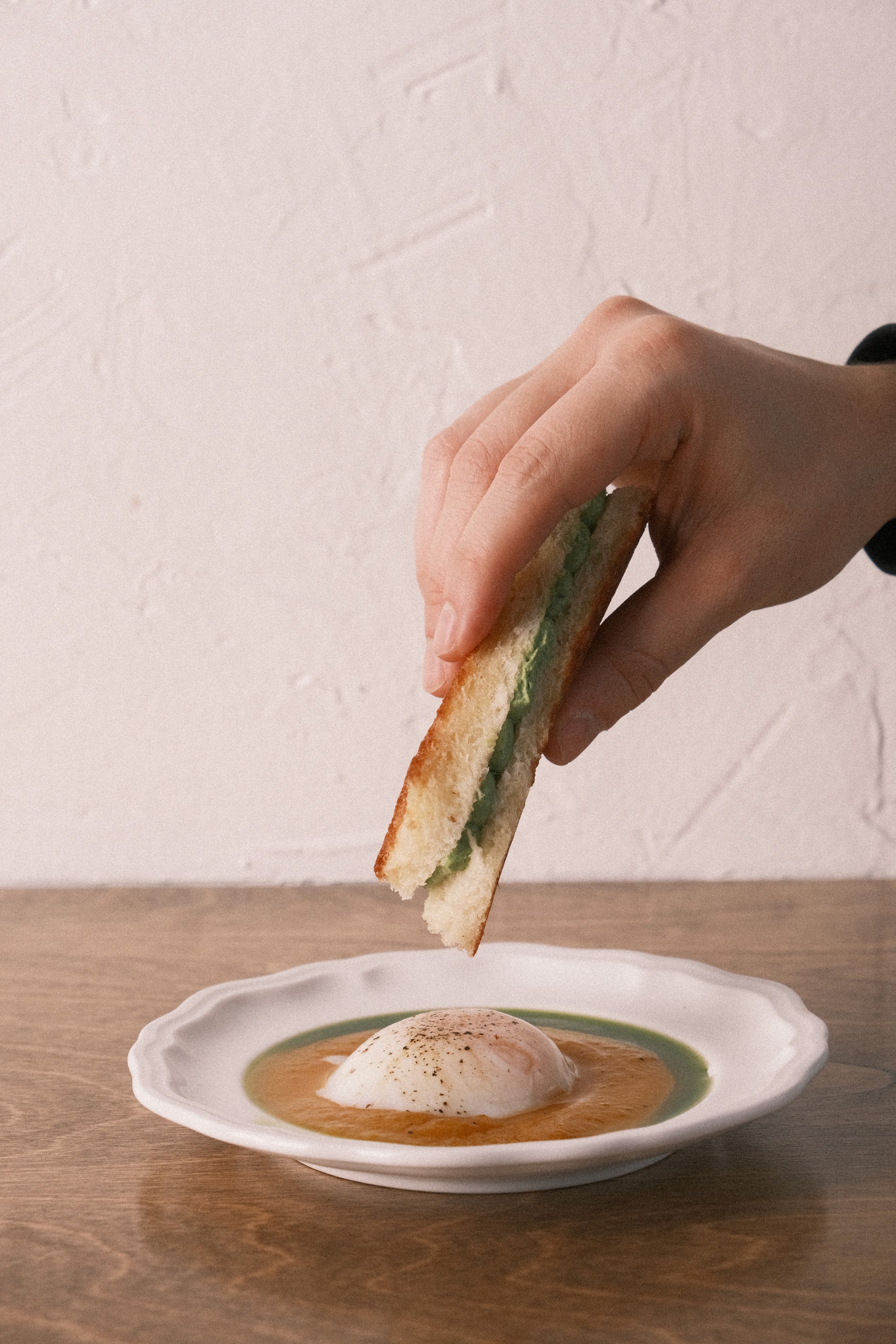 Une main trempe un pain brioché dans sa purée de courge et oeuf mollet.