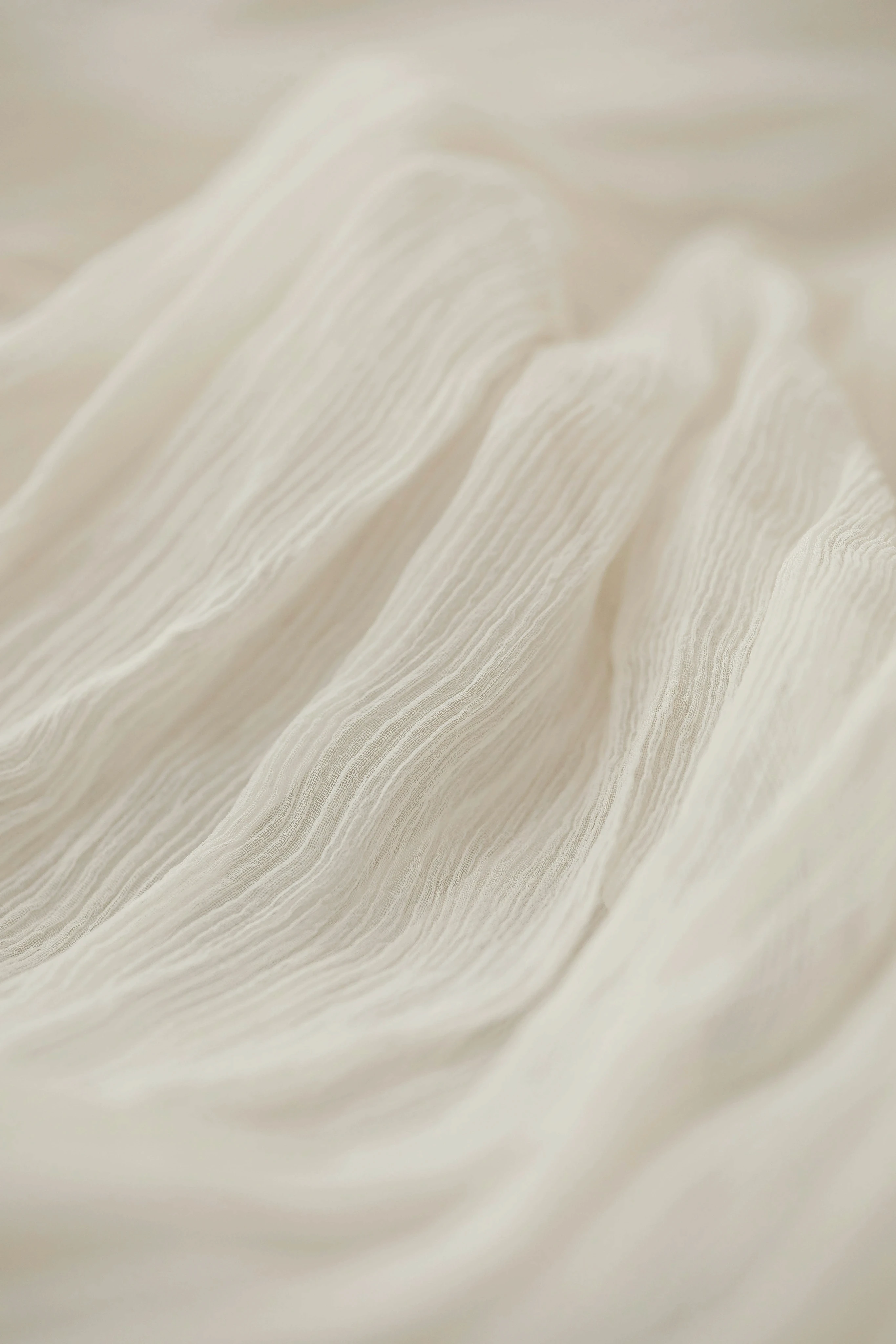 Close-up of elegant cream pleated silk fabric, highlighting high-quality texture and flow for luxury fashion.
