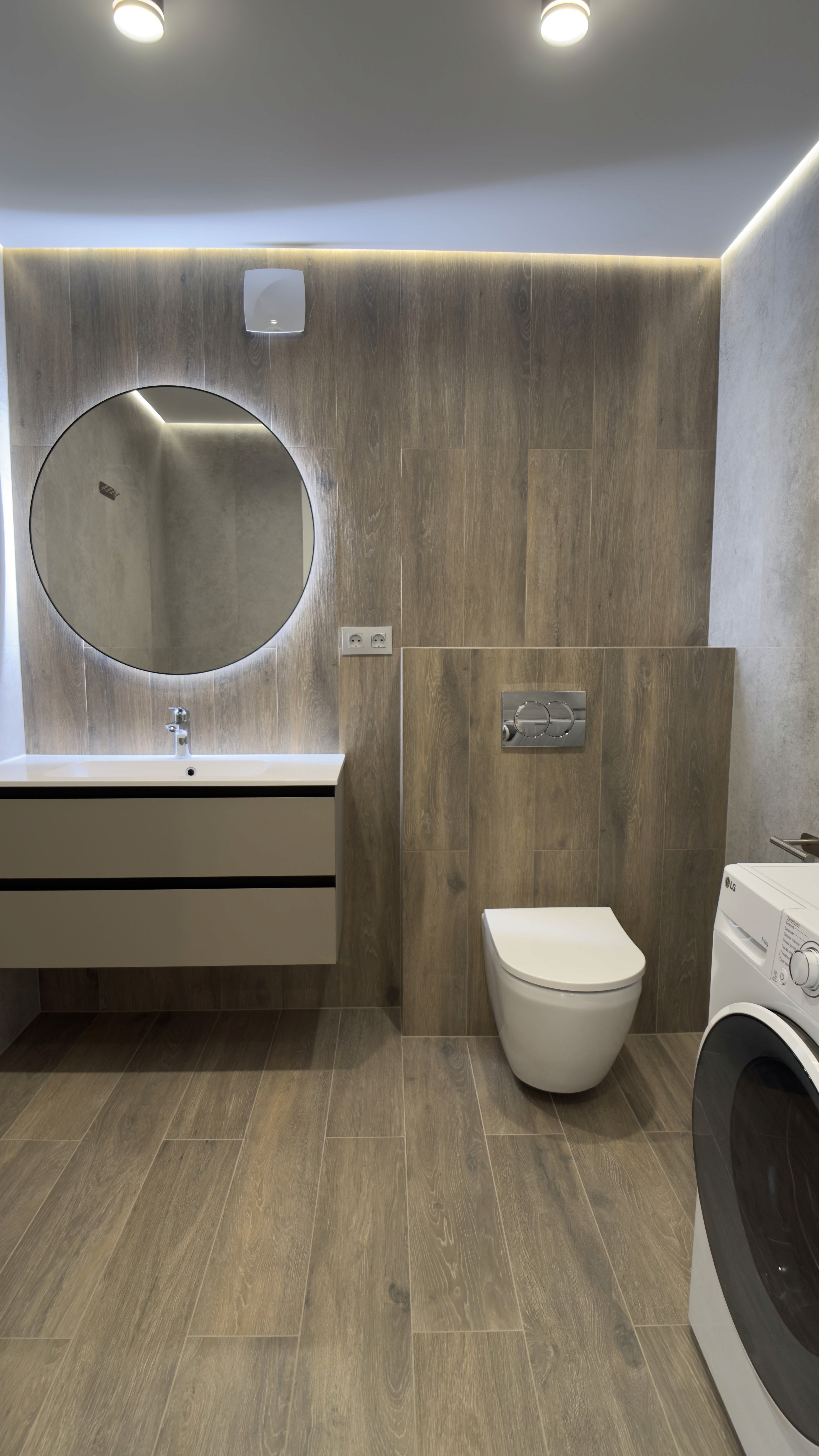 Санвузол з унітазом, пральною машиною, круглим дзеркалом і дерев’яним оздобленням