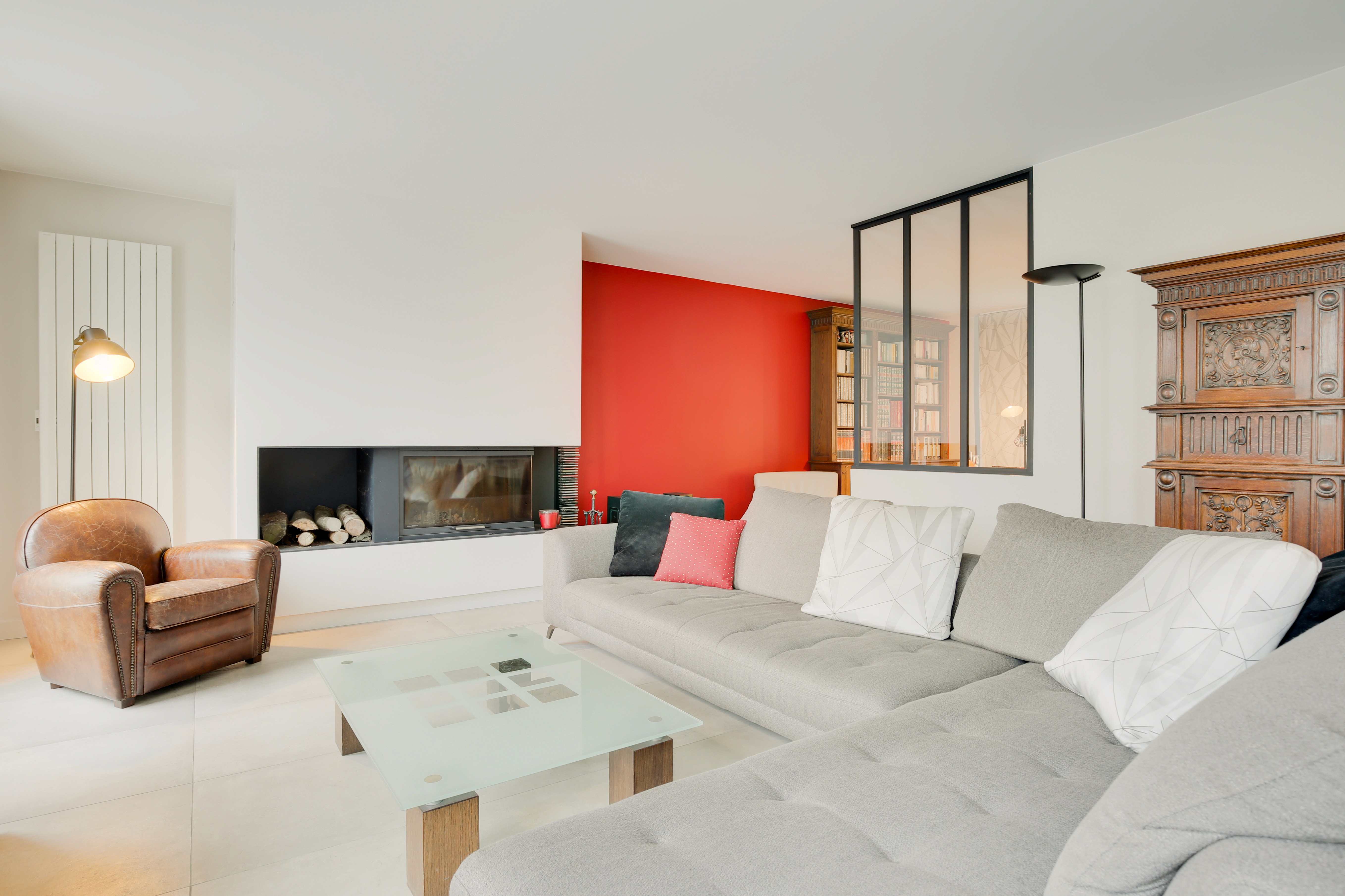 Rénovation salon Paris Est avec canapé sectionnel gris, fauteuil cuir marron, cheminée encastrée et mur accent rouge, architecte d'intérieur.