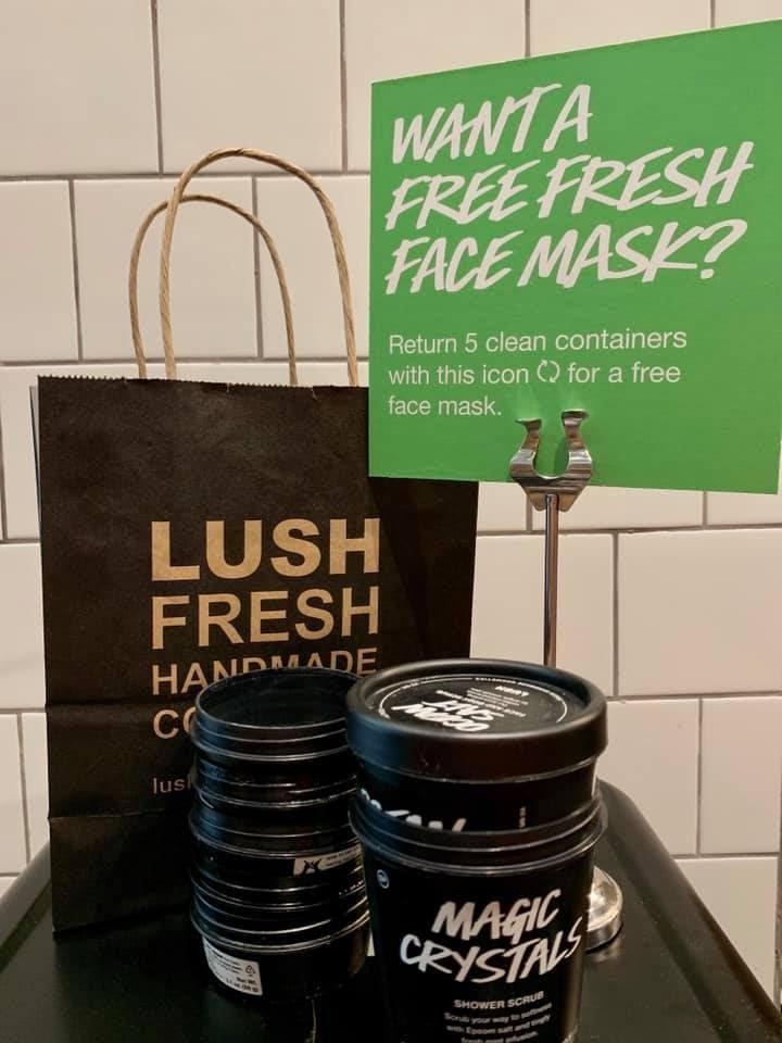Lush Fresh Handmade Cosmetics retail loyalty program example: green sign reading "Want a free fresh face mask? Return 5 clean containers with this icon for a free face mask" — illustrating a sustainability-based reward mechanic with empty container recycling incentive