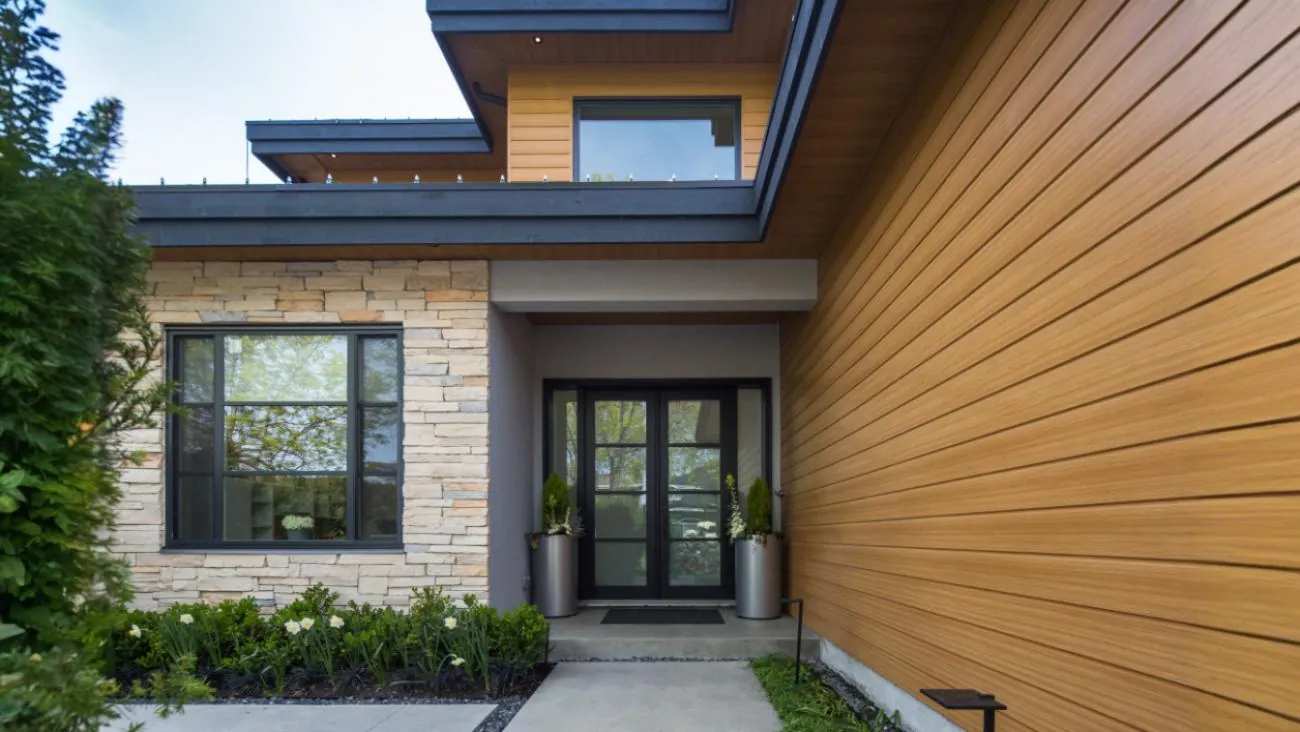 Elegant custom home front entrance with glass panel door, natural stone feature wall, horizontal wood siding, and professionally landscaped garden in Richmond