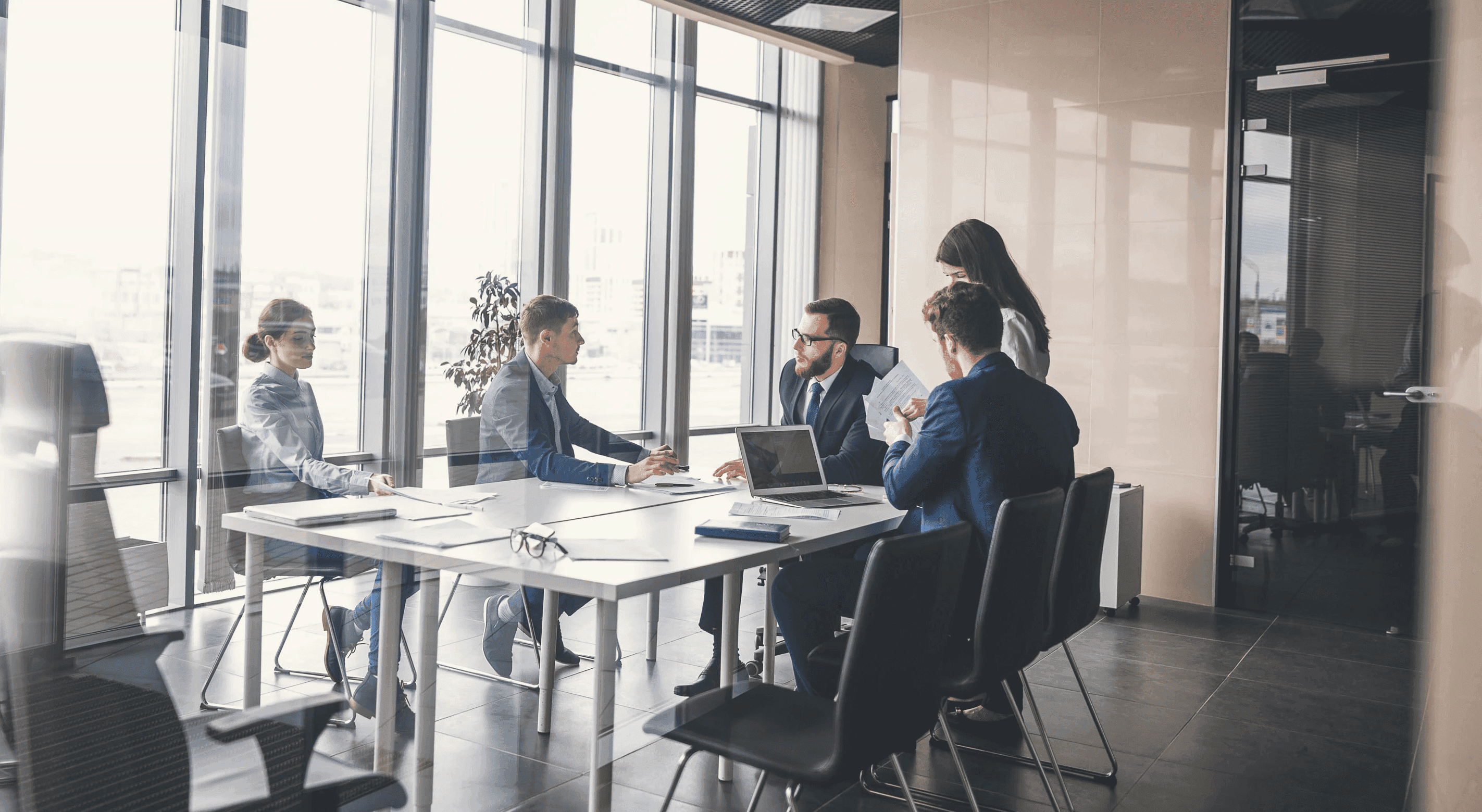 Board members meeting in a modern conference room reviewing documents and laptops, representing the key questions leadership teams must ask to ensure effective watchlist management.