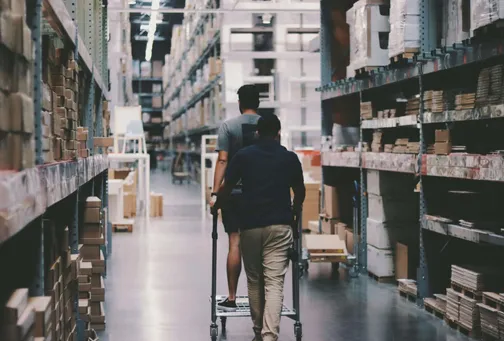 Mehrere Personen transportieren Waren mit einem Leiterwagen in einem Lager