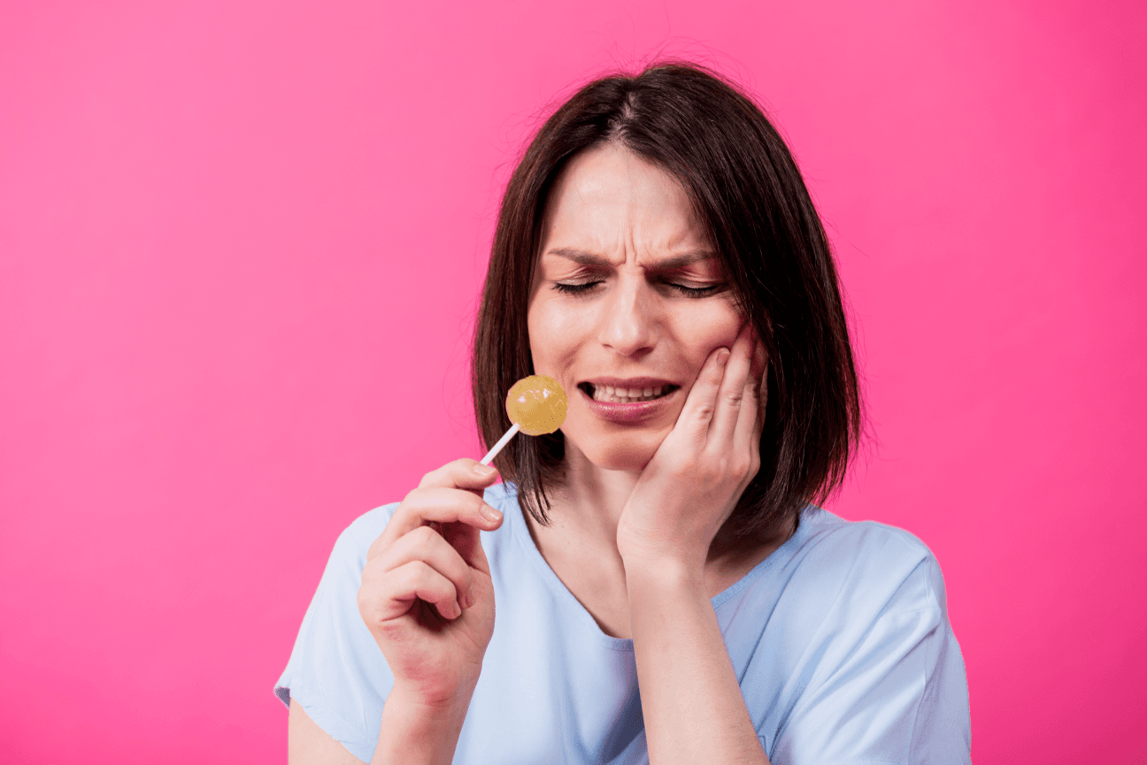 A woman holding a lollipop and wincing in pain, indicating tooth sensitivity or dental pain.