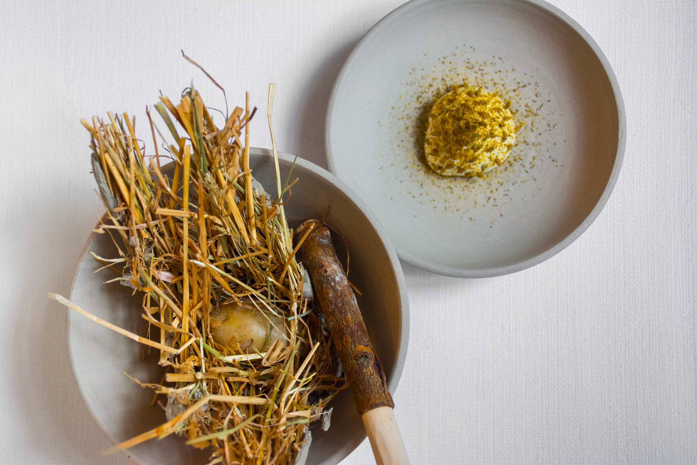 Dried yellow flowers and stems in one bowl next to a small mound of yellow powder on a second plate.