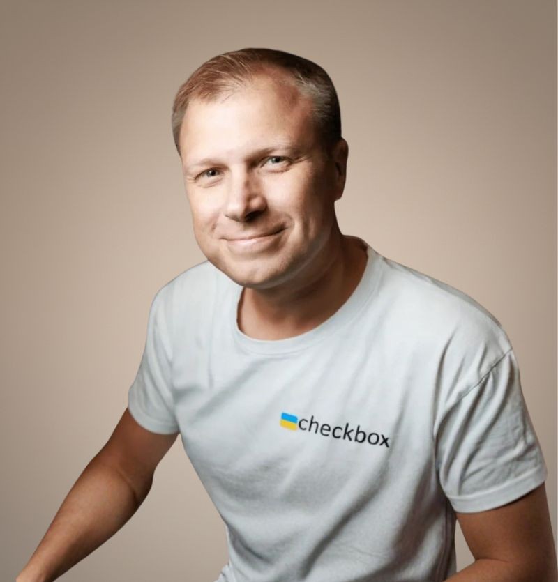A confident person with short, styled hair and a leather jacket poses against a dark backdrop.