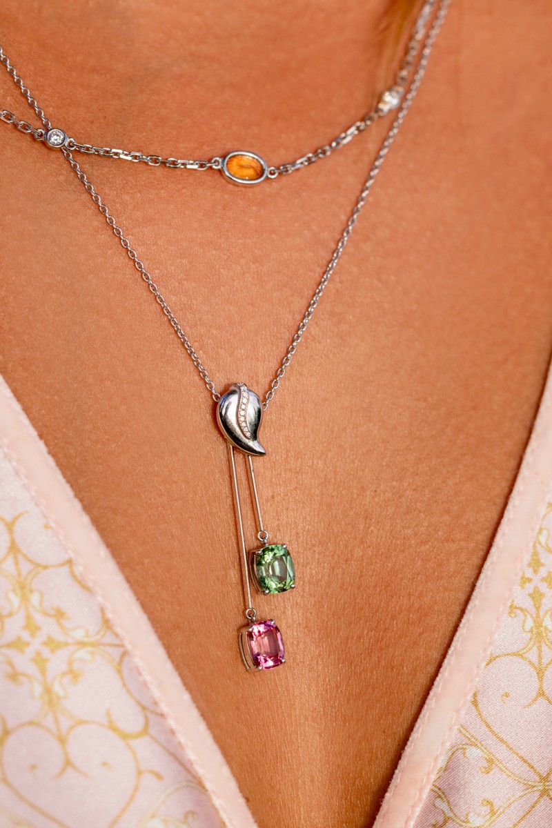 Close-up of a woman’s neckline adorned with Manos de Oro Saint Barth handcrafted luxury necklaces—featuring a silver seashell pendant with sparkling diamonds and two radiant cushion-cut gemstones, symbolizing refined elegance and soulful island artistry.