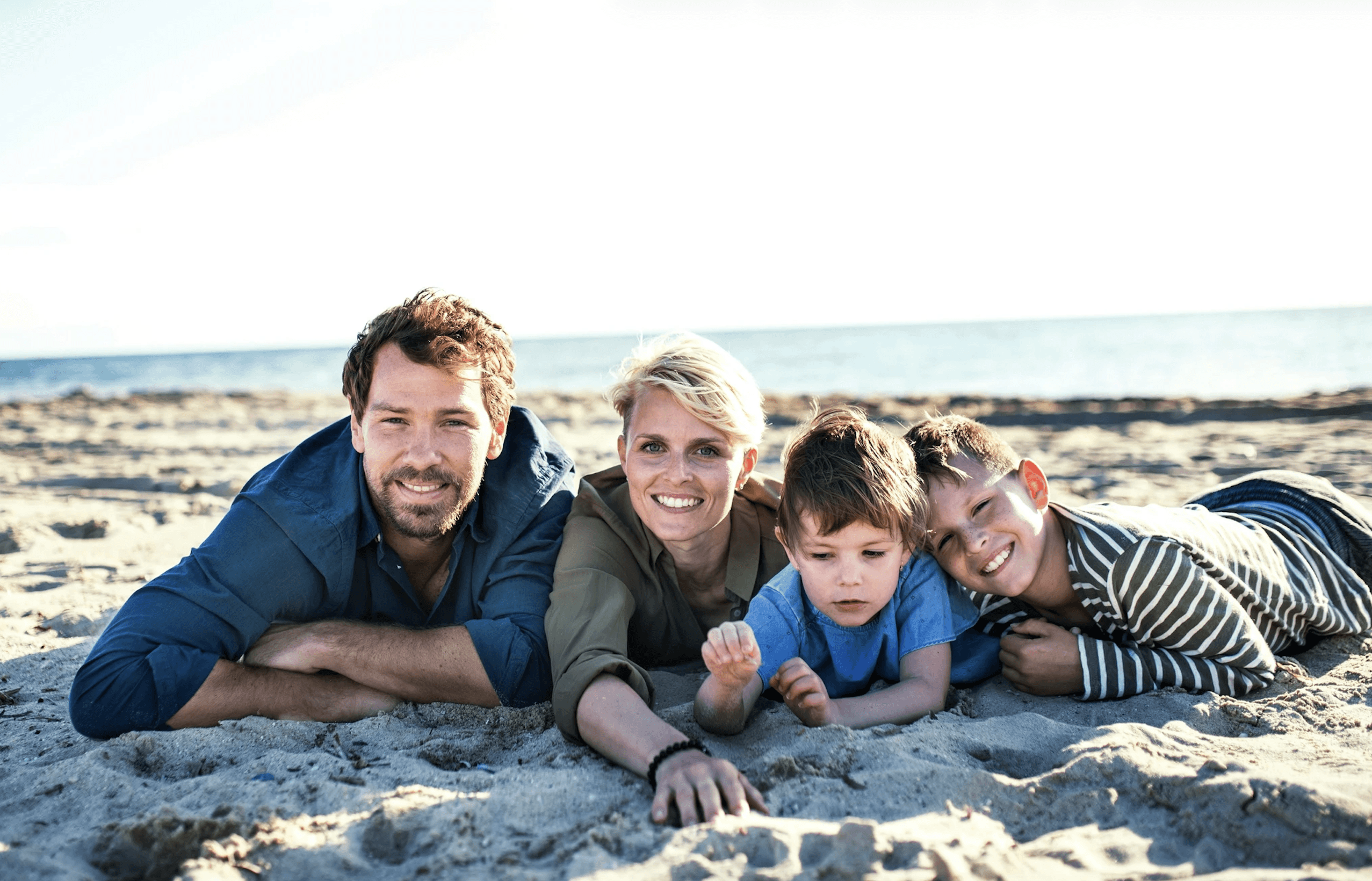 two adults and children lying in sand on a beach