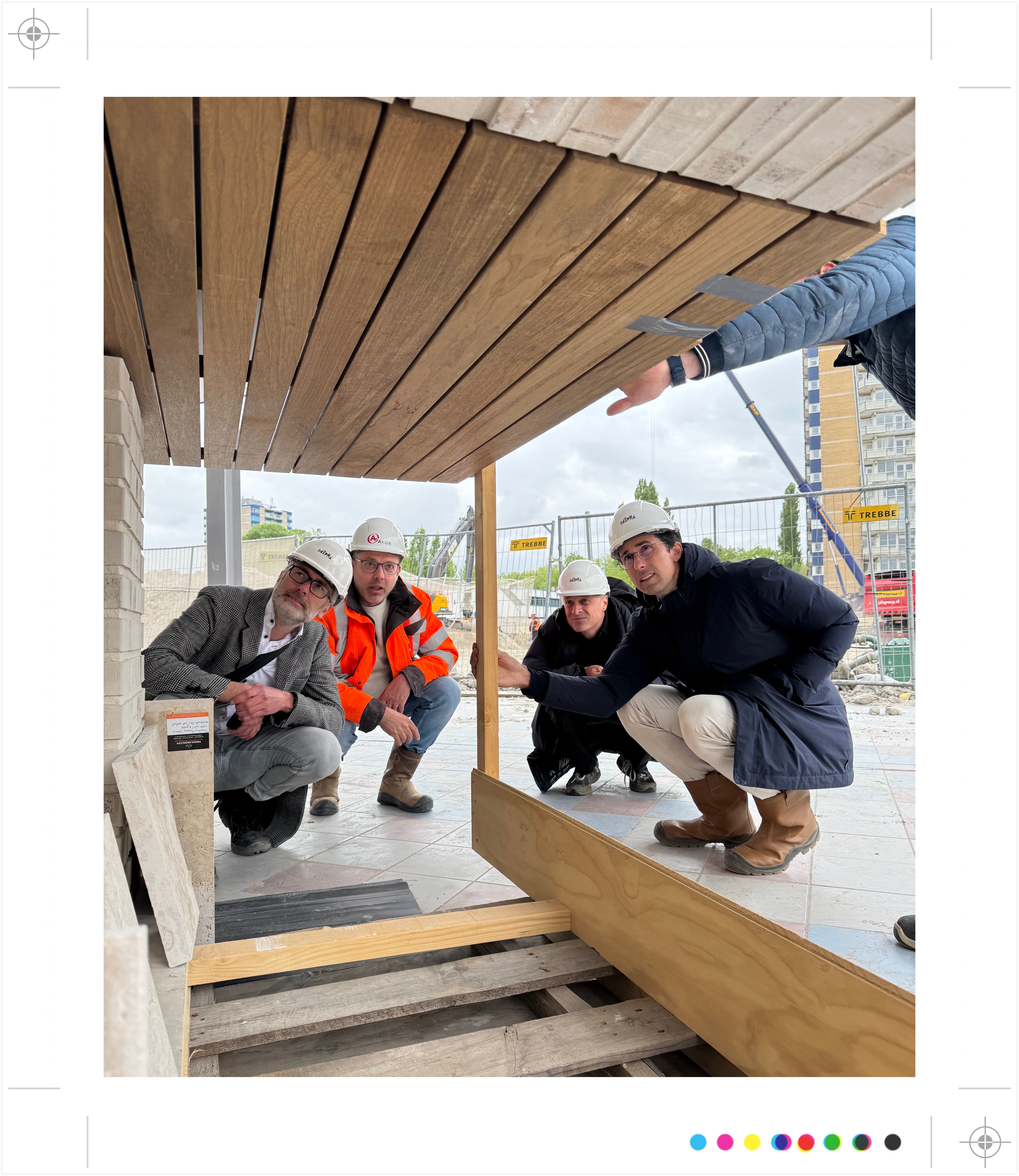 Vier personen met helmen inspecteren een bouwproject, knielend en wijzend.