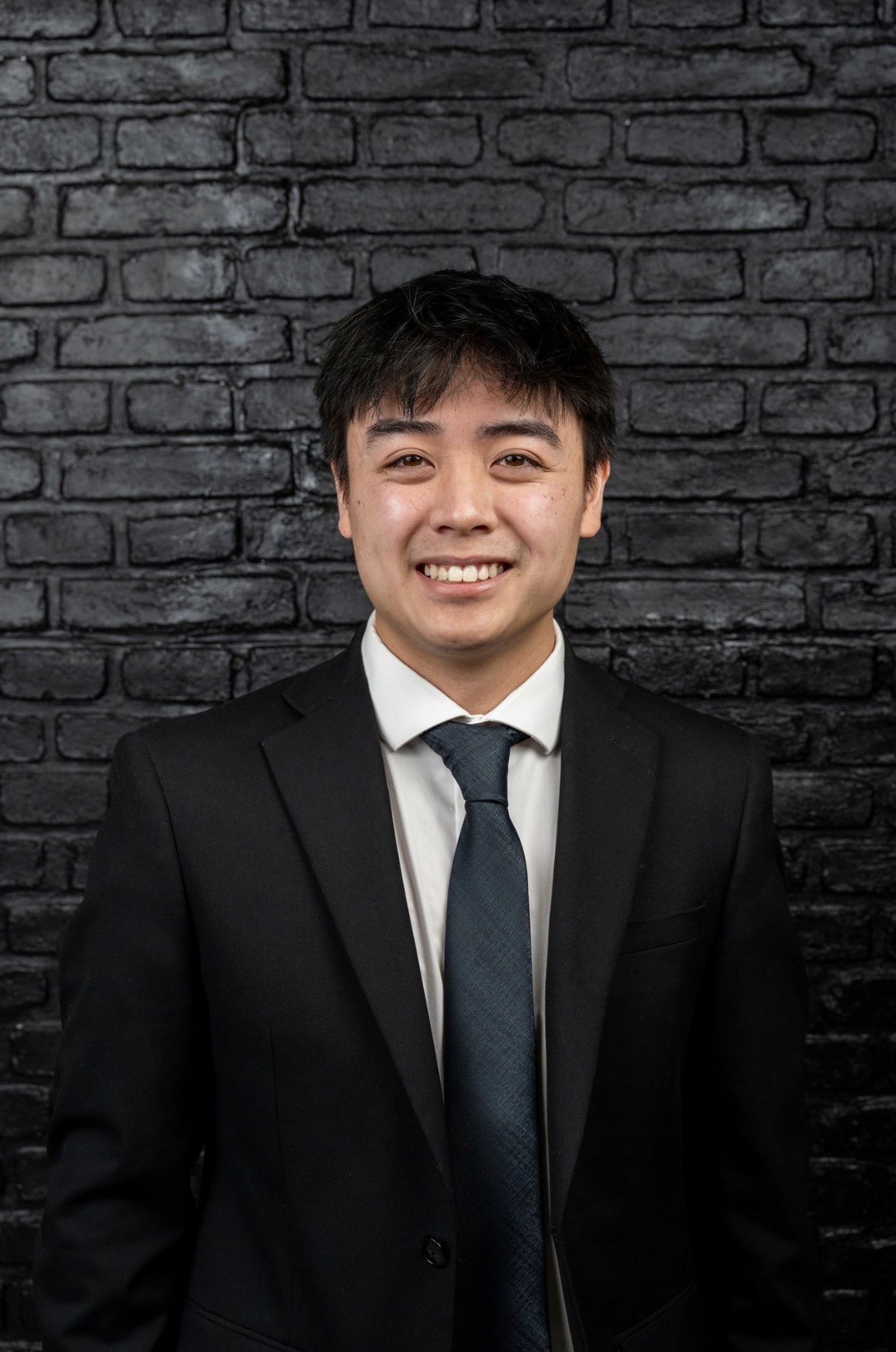 A thoughtful young person with dark hair gazes to the side, captured in soft black and white lighting.