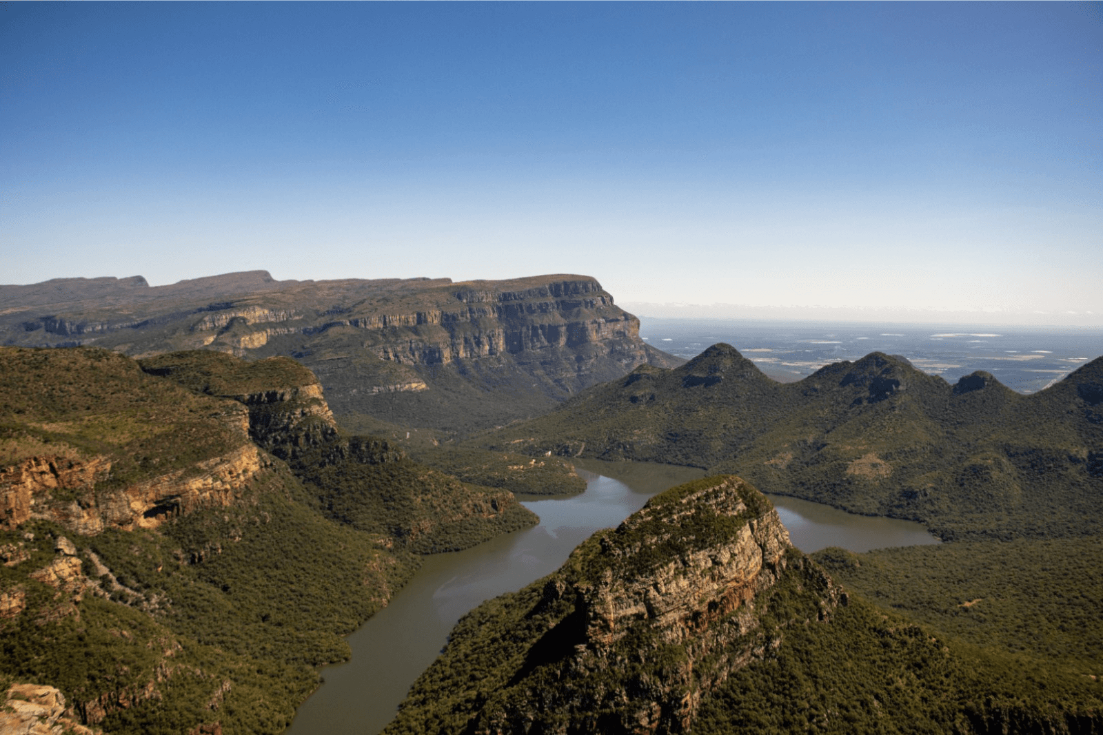 Vue panoramique du Blyde River Canyon montrant des montagnes couvertes de végétation dense et une rivière serpentant entre les falaises rocheuses.