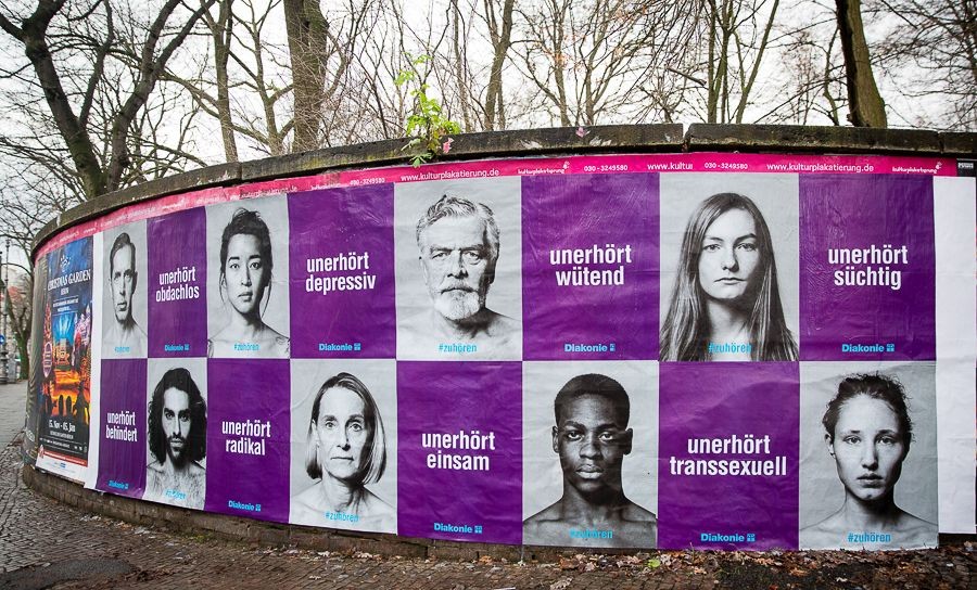 A wall of posters alternating between portraits of people and bold slogans such as “Outrageously angry,” “Outrageously lonely,” “Outrageously transgender,” and others. The photo was taken by Kathrin Harms. Image rights are held by Diakonie.