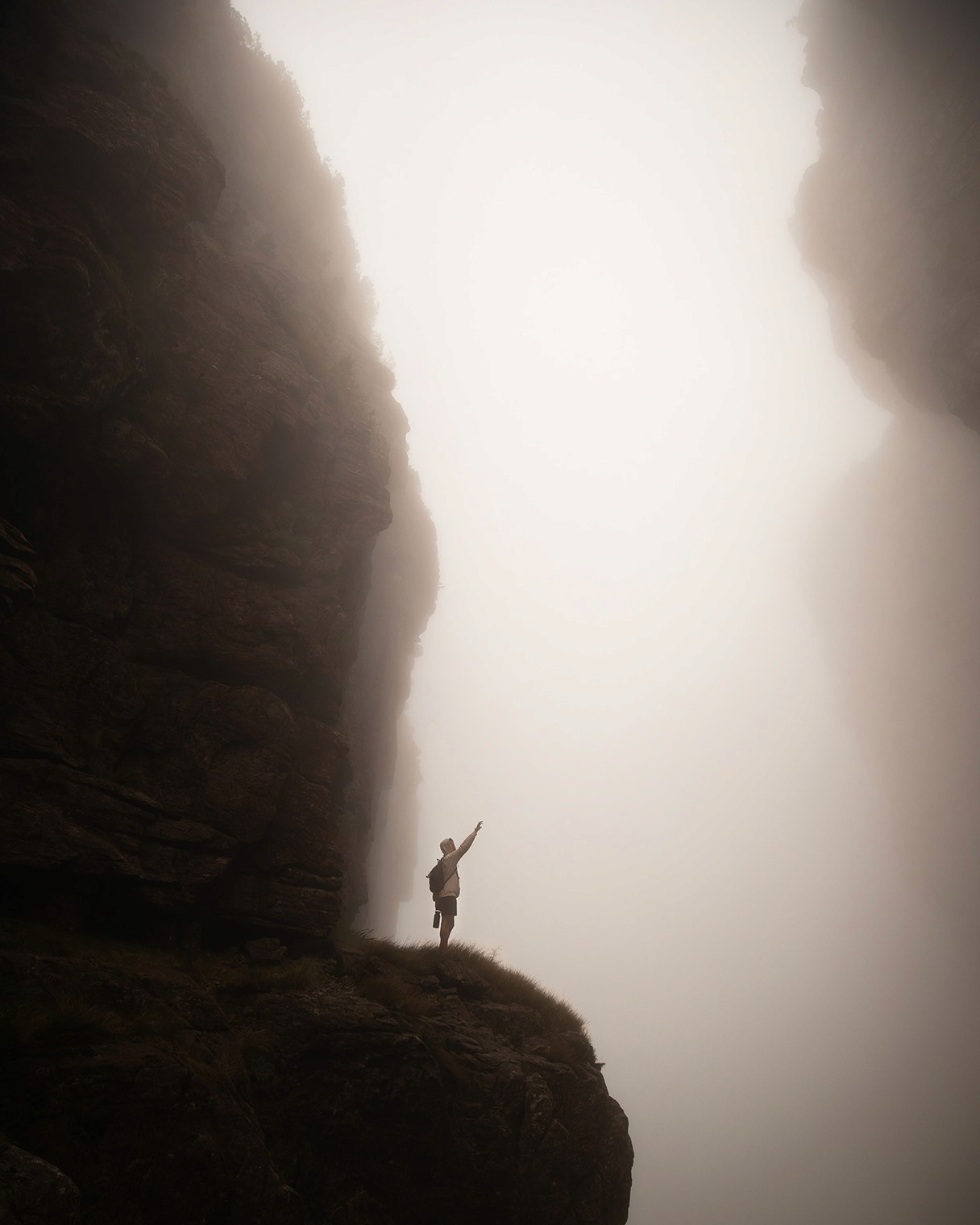 Foggy cliffside with a person standing on the edge, fog covering the right side.