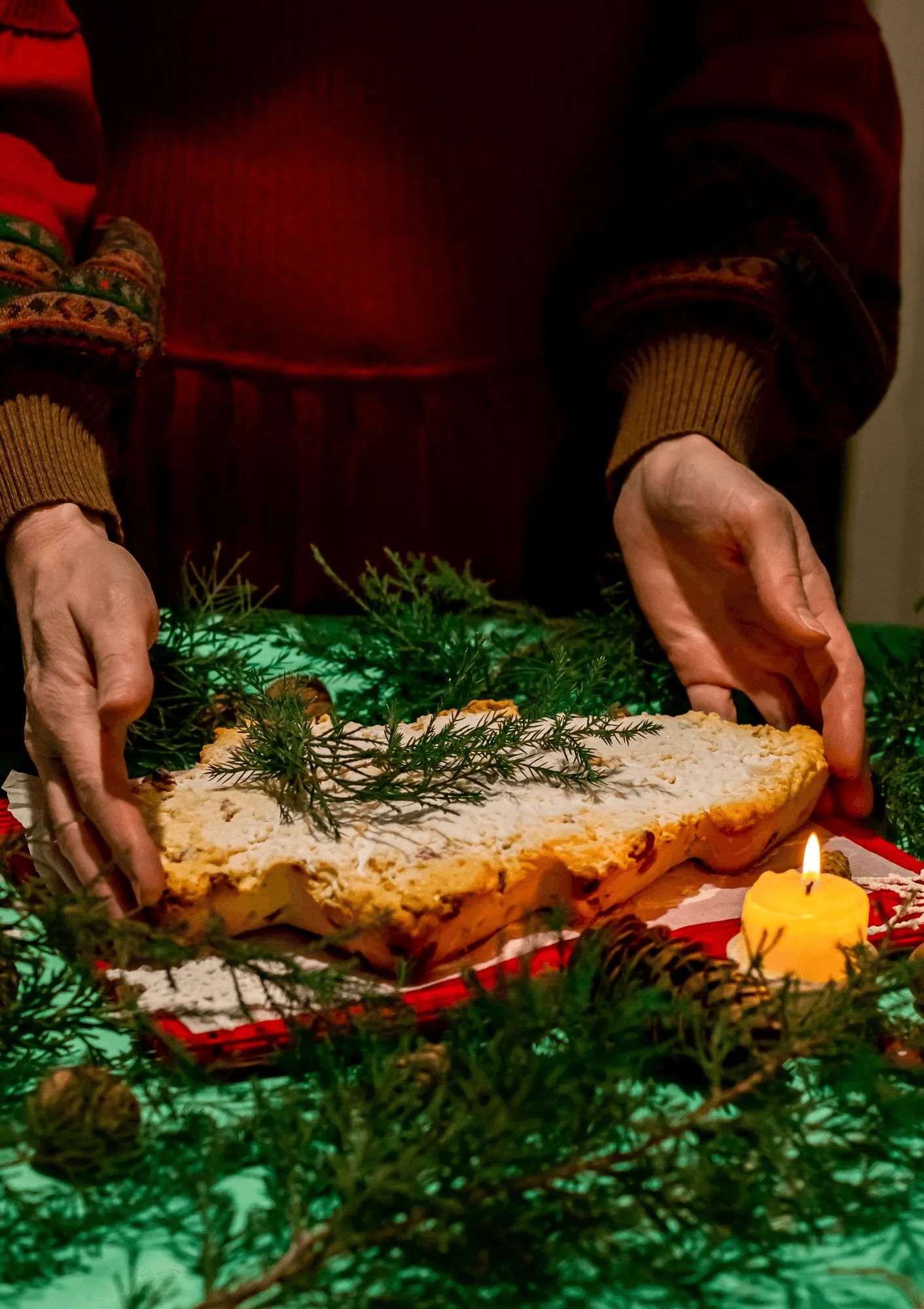 Hands placing Christmas bread on a festive table with a candle