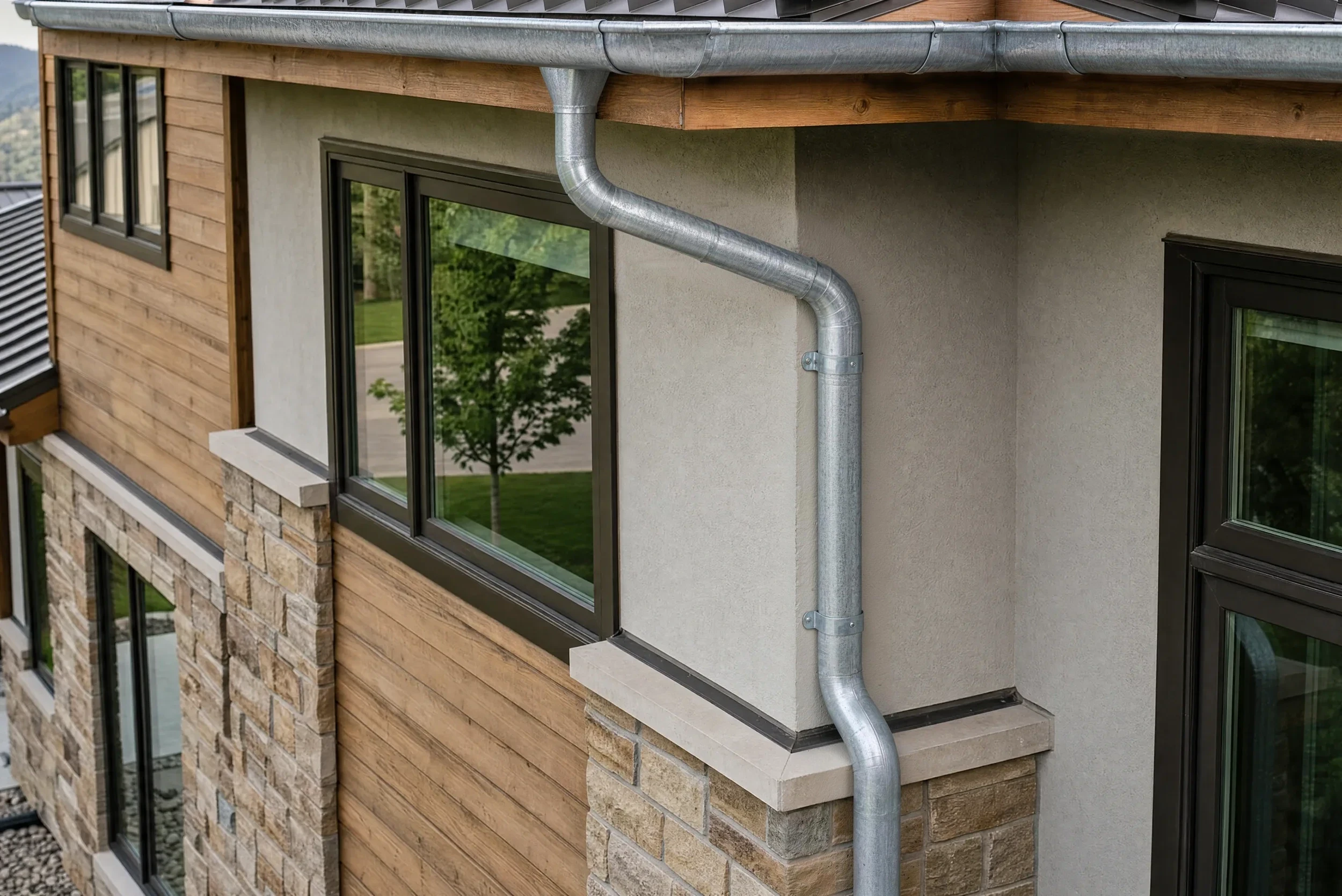 Half-round galvanized steel gutter and smooth round downspout on a home with wood siding, stucco, and stone