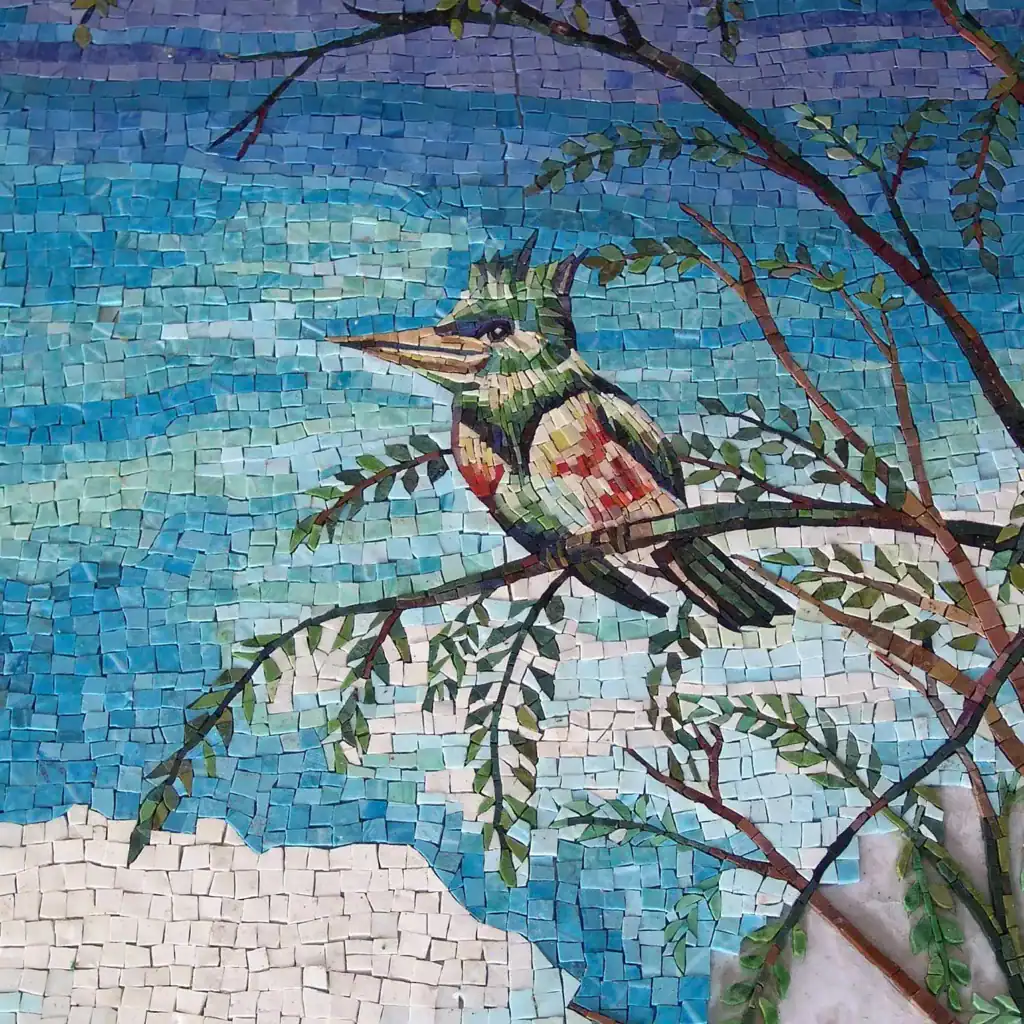 Colorful mosaic hummingbird perched on a branch against a blue sky background.