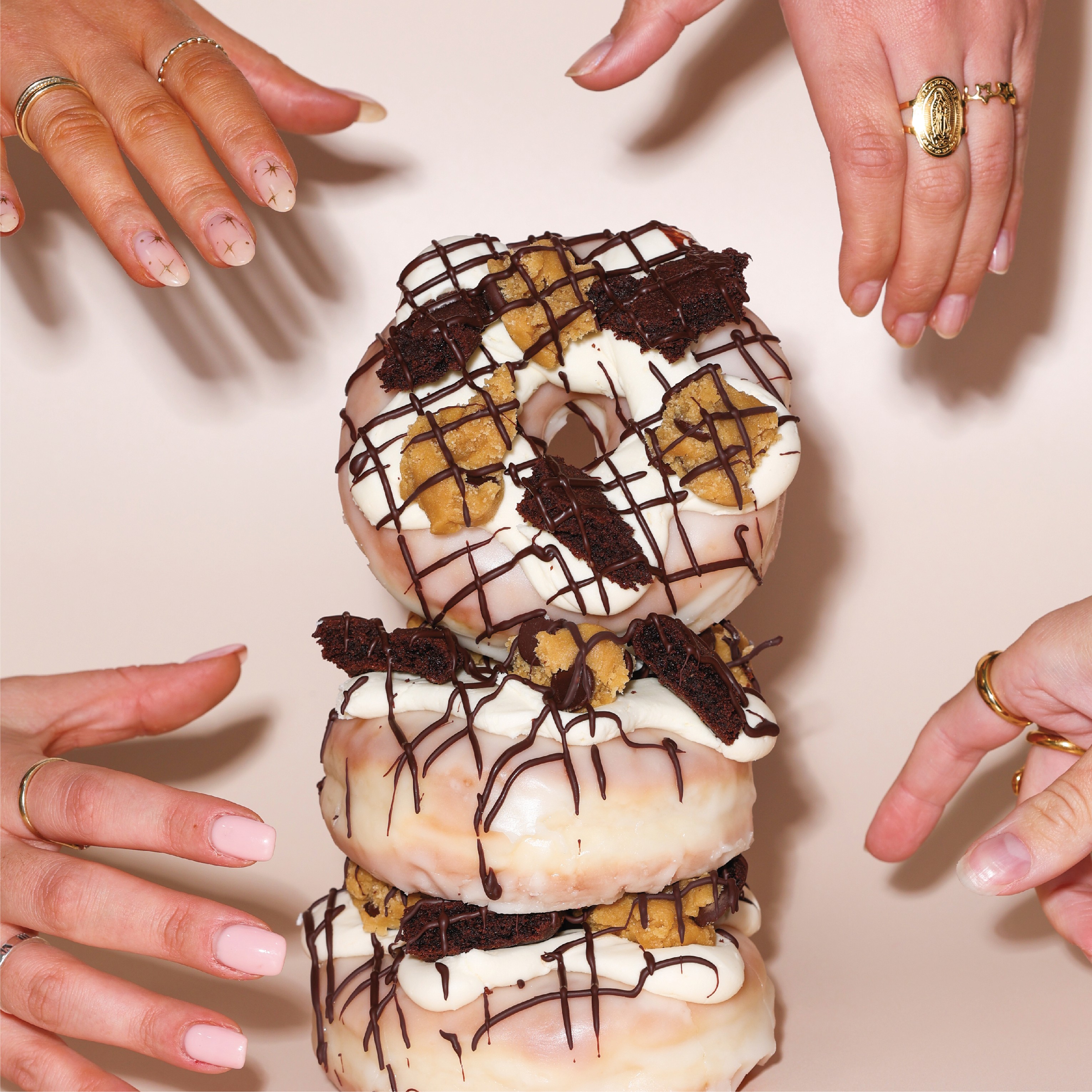 Multiple hands reaching to grab a tower of doughnuts
