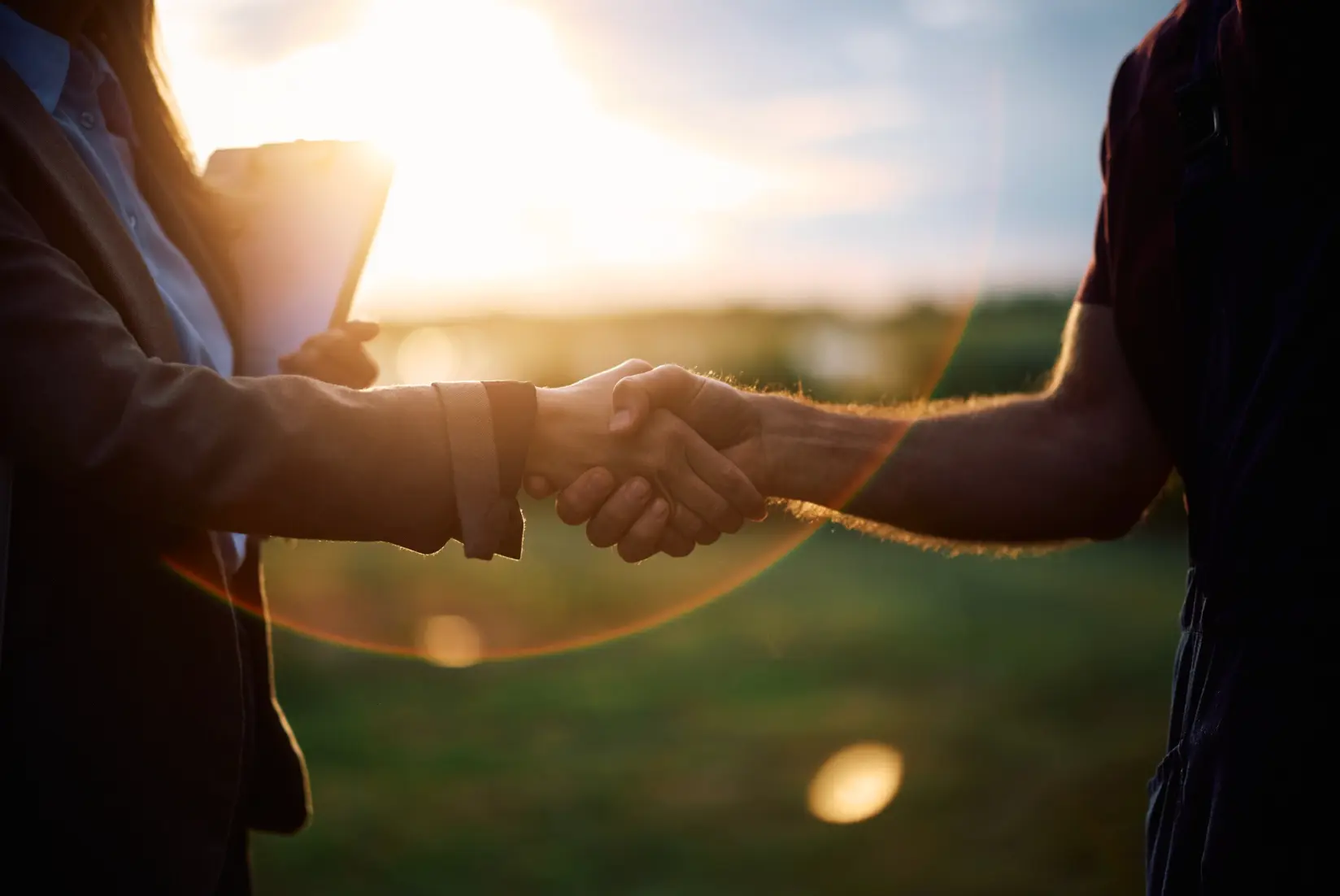 Close-up of a business handshake silhouetted against a sunset, illustrating the formation of a strategic business partnership