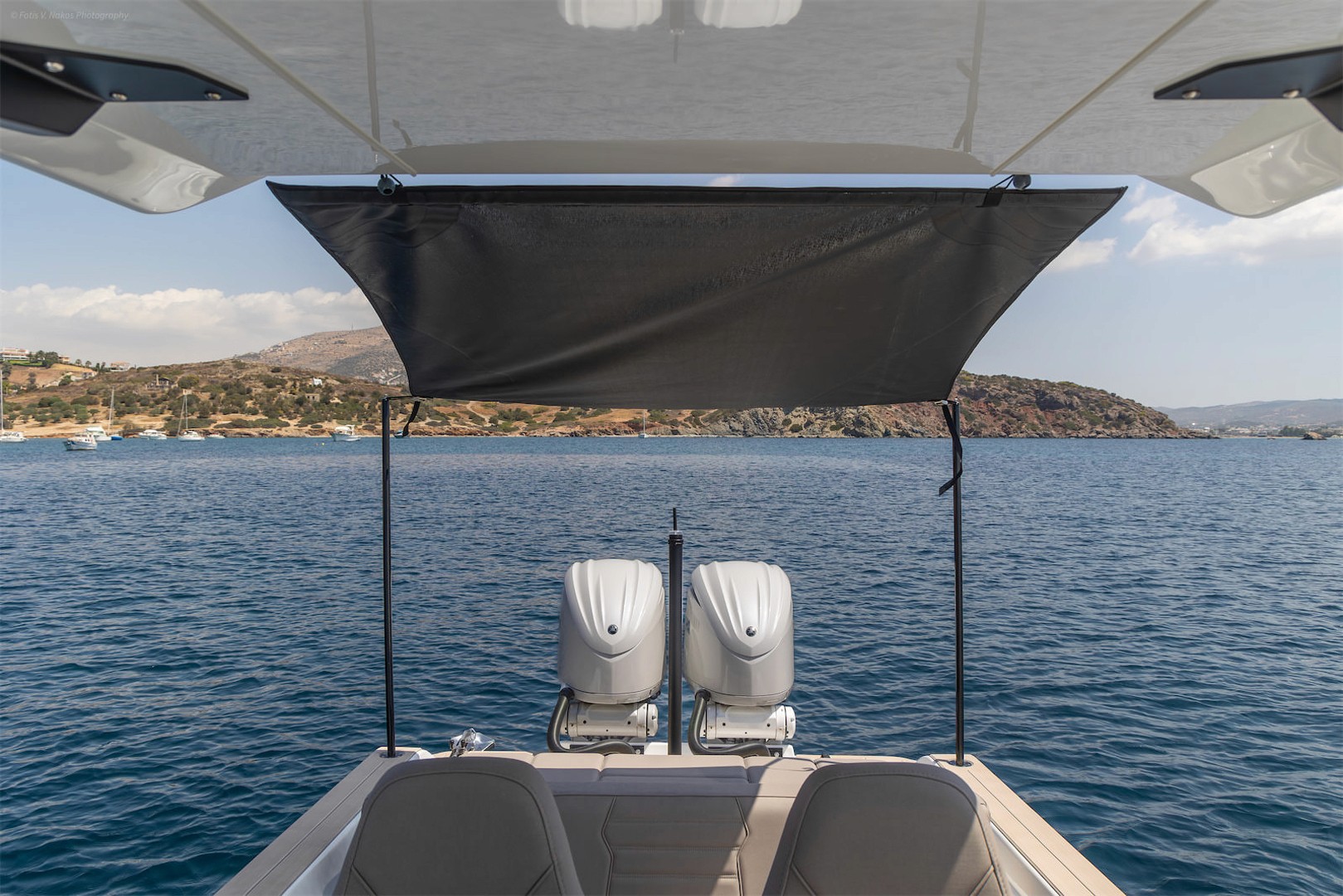White speedboat with open cabin hatch revealing interior seating, anchored in calm turquoise waters near rocky cliffs in the Cyclades.
