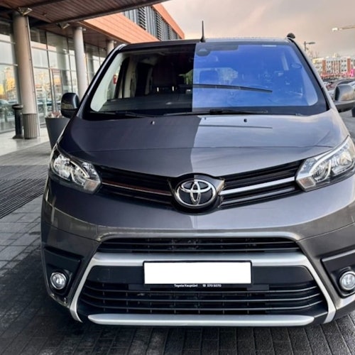 Miniván Toyota gris estacionada frente a un edificio moderno con grandes ventanas y un voladizo de madera.