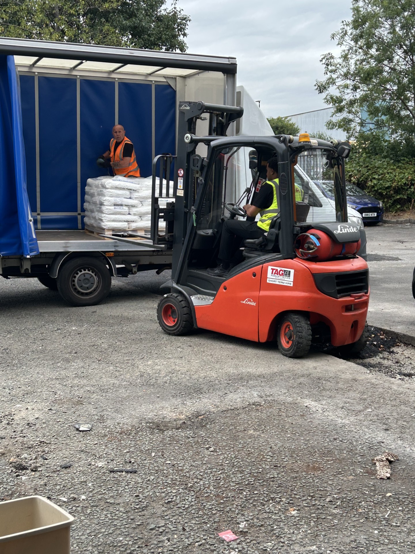 Image of a forklift driver in high vis loading a luton van with a pallet and a man inside the van in a high vis helping load the van