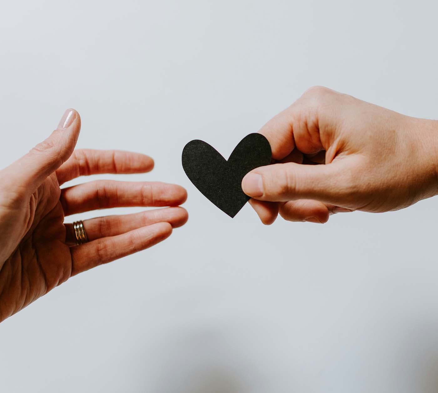 Two hands reaching towards each other with one holding a black heart.