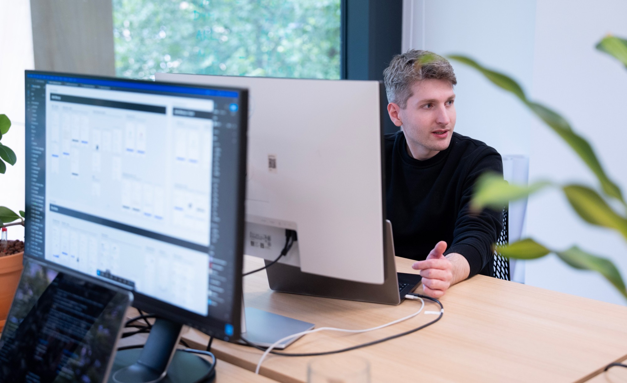 Two colleagues at a desk discussing an app interface on a monitor as one turns to talk to the other