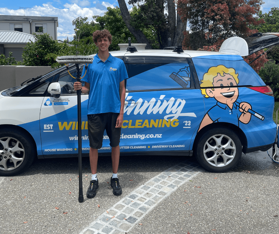 Team member standing with window cleaning tools beside branded Winning Window Cleaning car