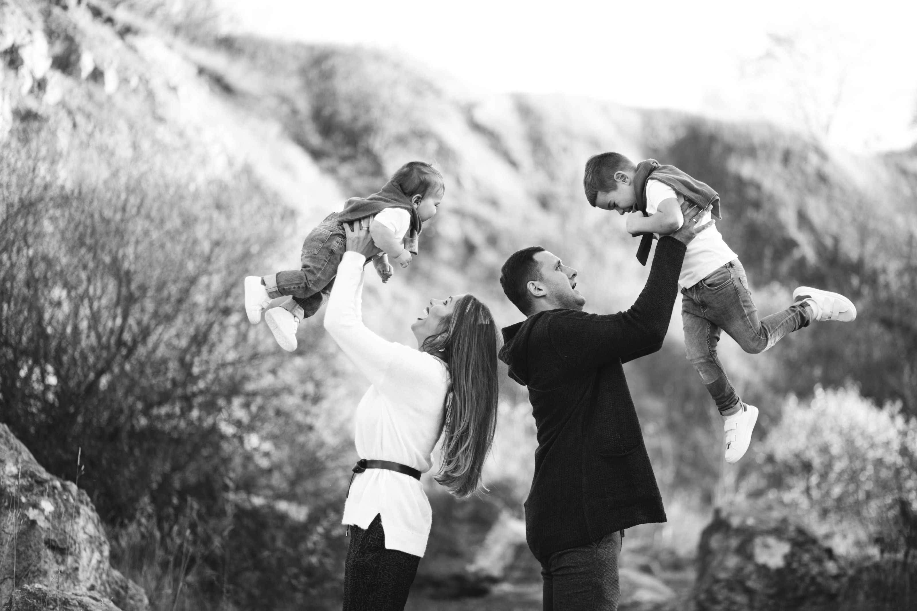 Black and white family photos of parents lifting kids outdoors