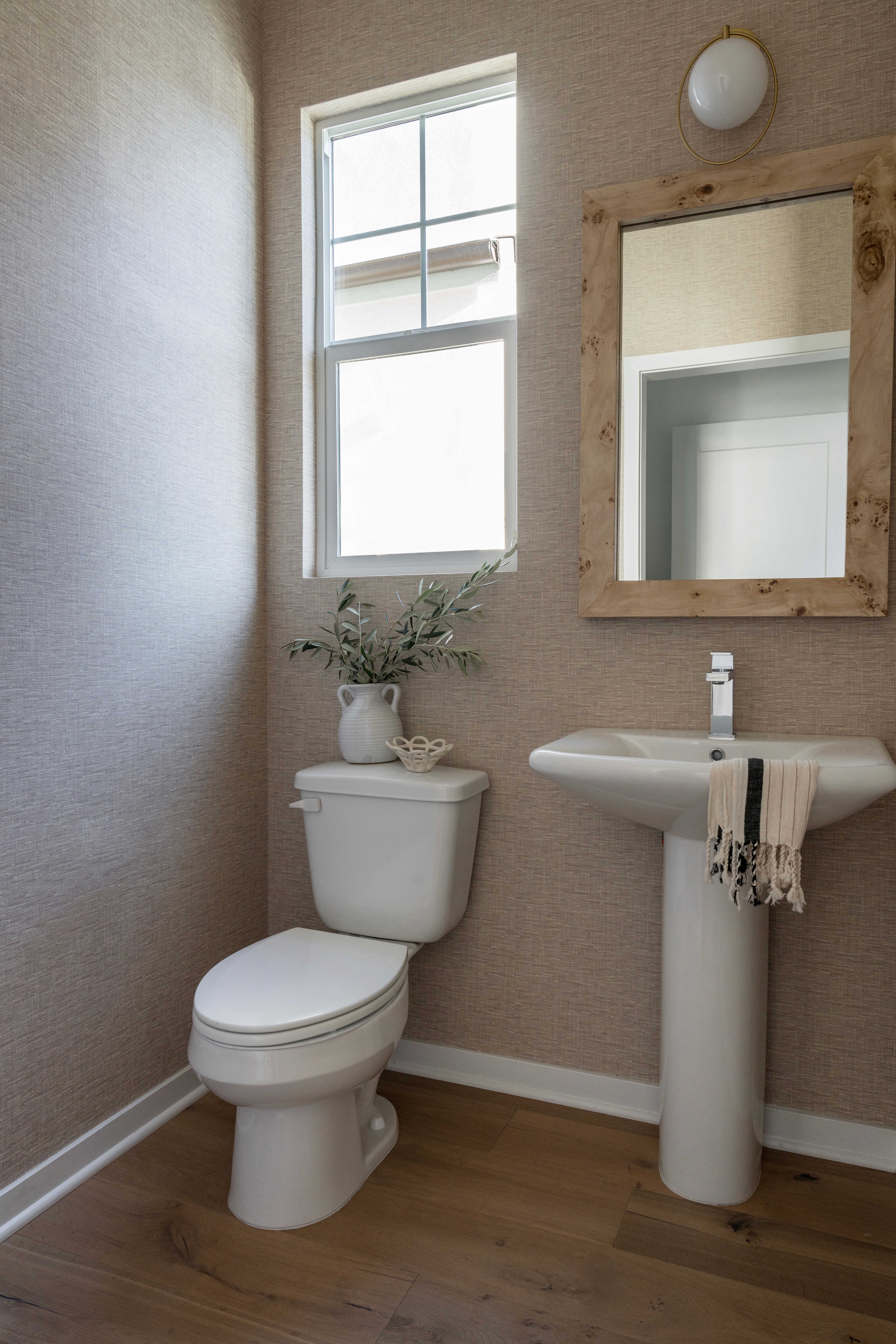 Neutral toned powder room with wood framed mirror, wood flooring, and white pedestal sink by Jubilee Interiors in Arcadia, California