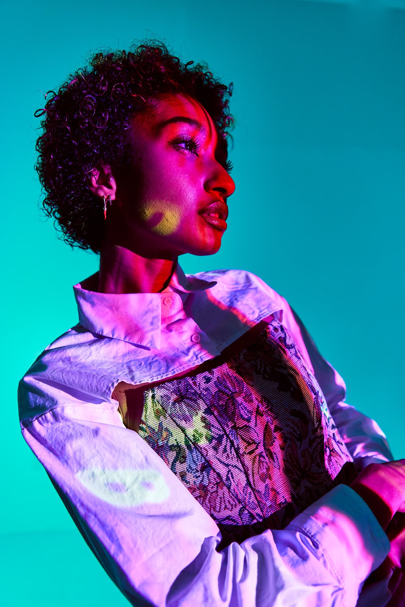 A side profile of the model’s face is illuminated by pink and yellow light against a turquoise backdrop at Revelator Studio, Shreveport’s premier natural light photography studio.