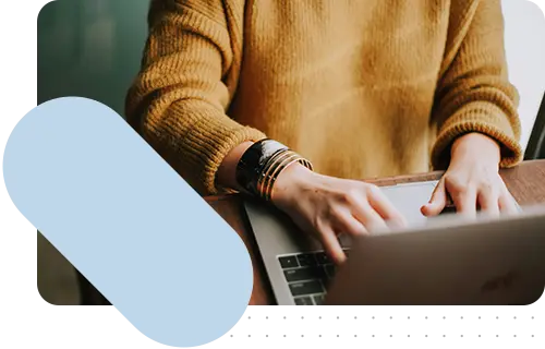 A person with a yellow sweater typing on a laptop, with a blue accent in the corner of the image.