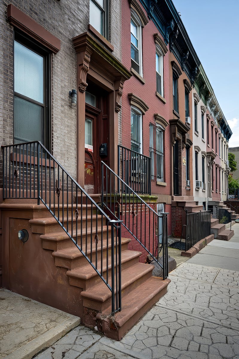 Charming row of urban brownstone buildings with ornate details, iron railings, and textured sidewalks on a sunny day.