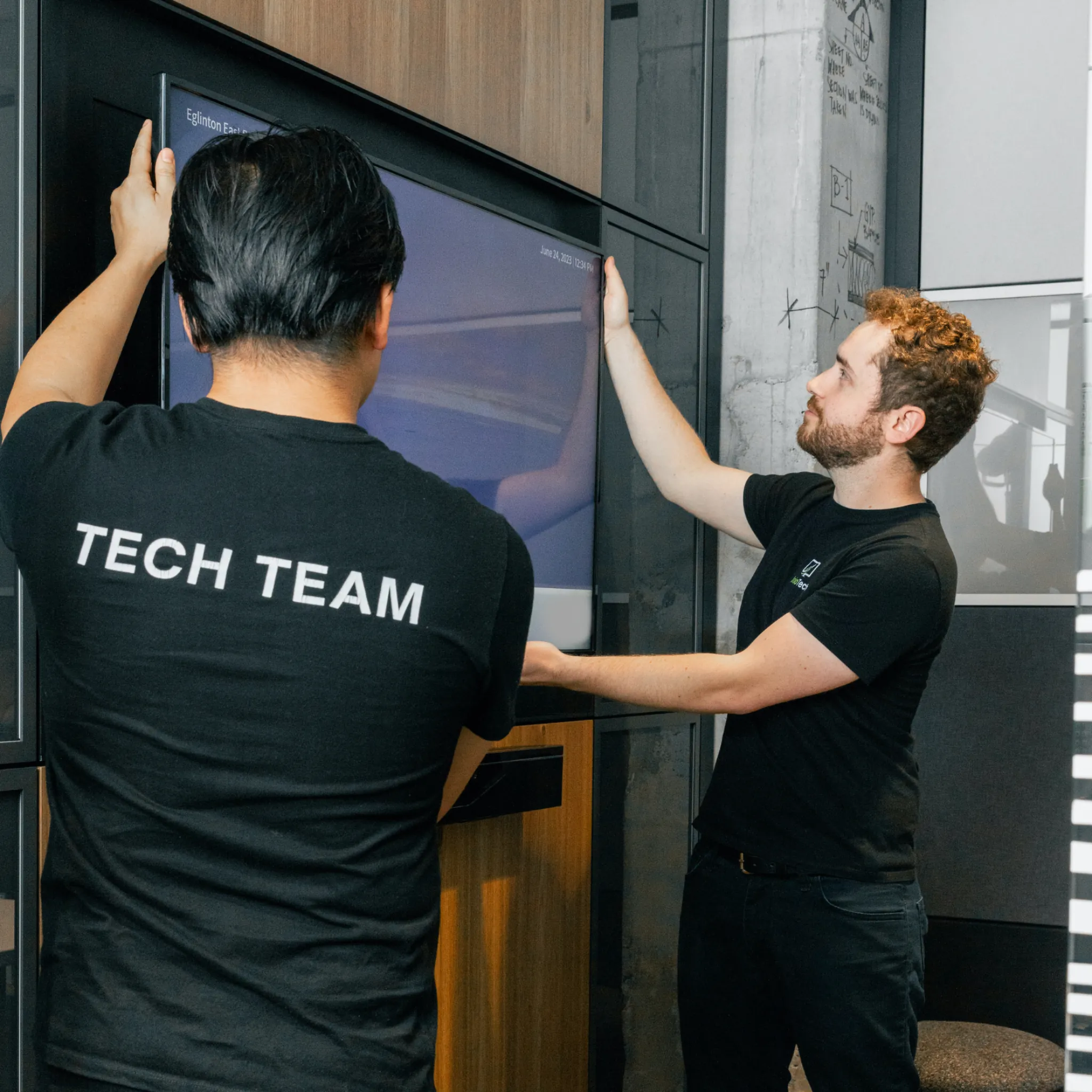 Technicians installing a wall-mounted display screen in a modern office, showcasing professional AV installation services