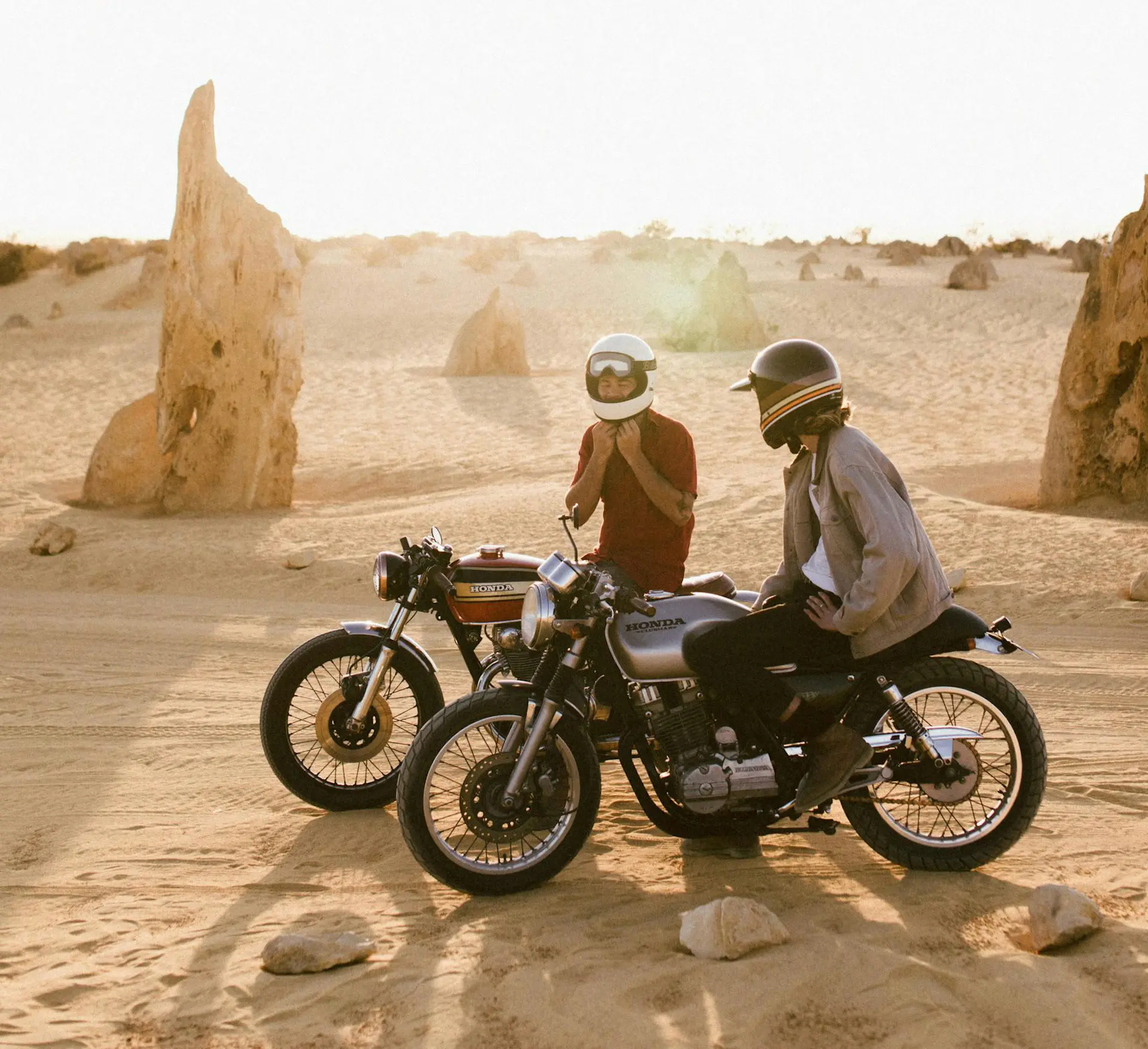 Deux motards faisant une pause dans un décor désertique, échangeant ensemble autour de leurs motos.